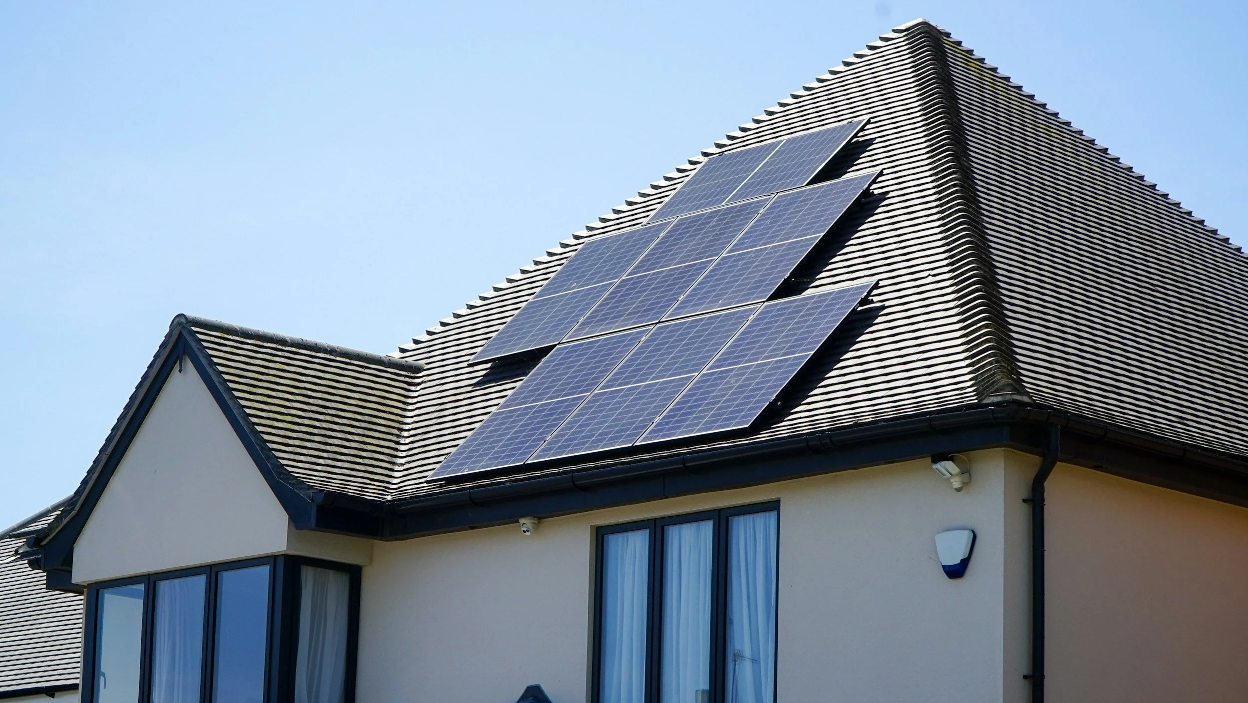 A house with a sloped roof featuring solar panels installed on one side, under a clear blue sky.