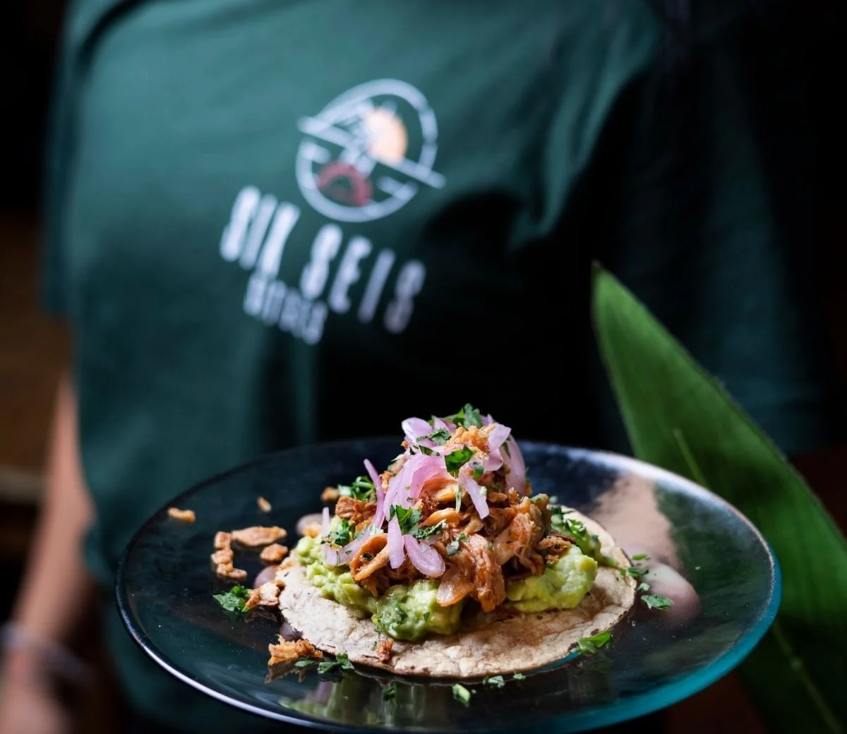 Taco topped with guacamole, shredded filling and pickled red onion at Six Seis Taquería