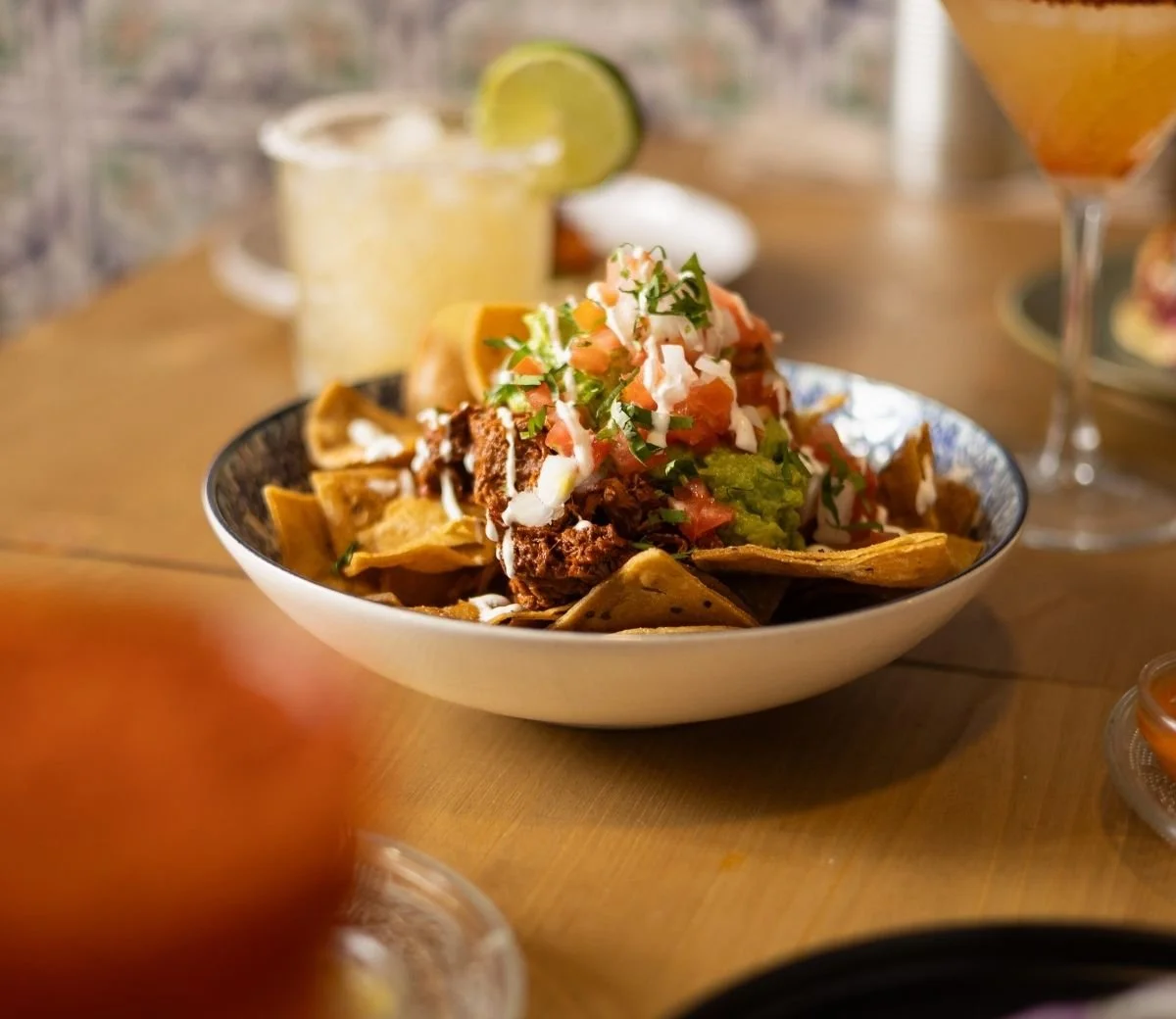 Nachos topped with guacamole, salsa and cream alongside a cocktail at Six Seis