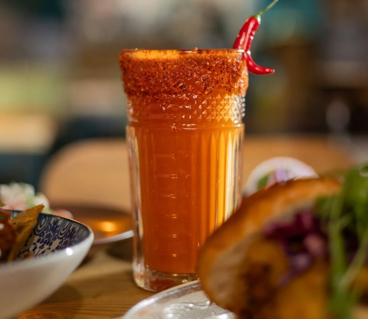 Tall red cocktail with a chilli rim and red chilli garnish at Six Seis