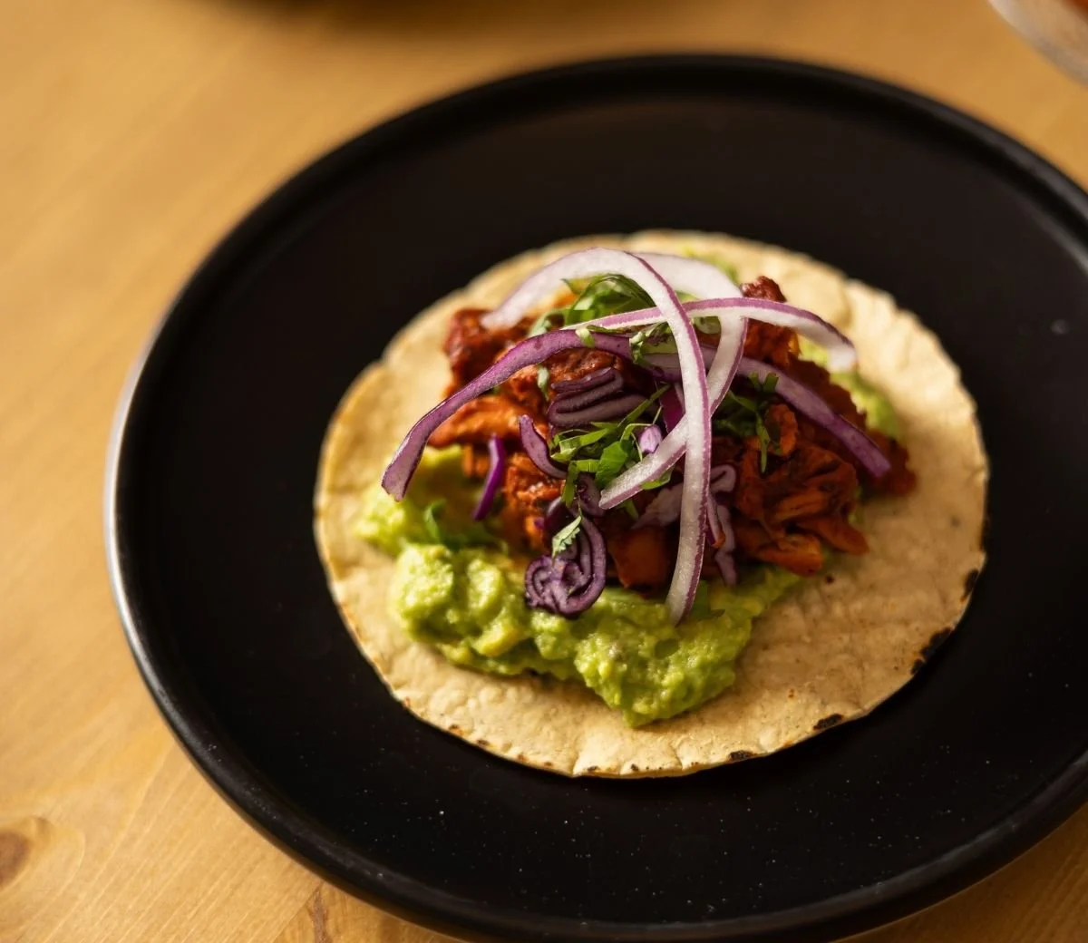 Mexican taco with guacamole and pickled red onion on a black plate at Six Seis