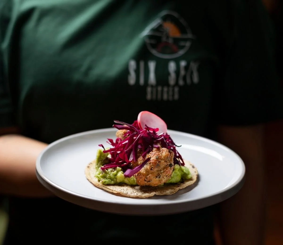 Taco topped with pickled red onion, served on a white plate at Six Seis