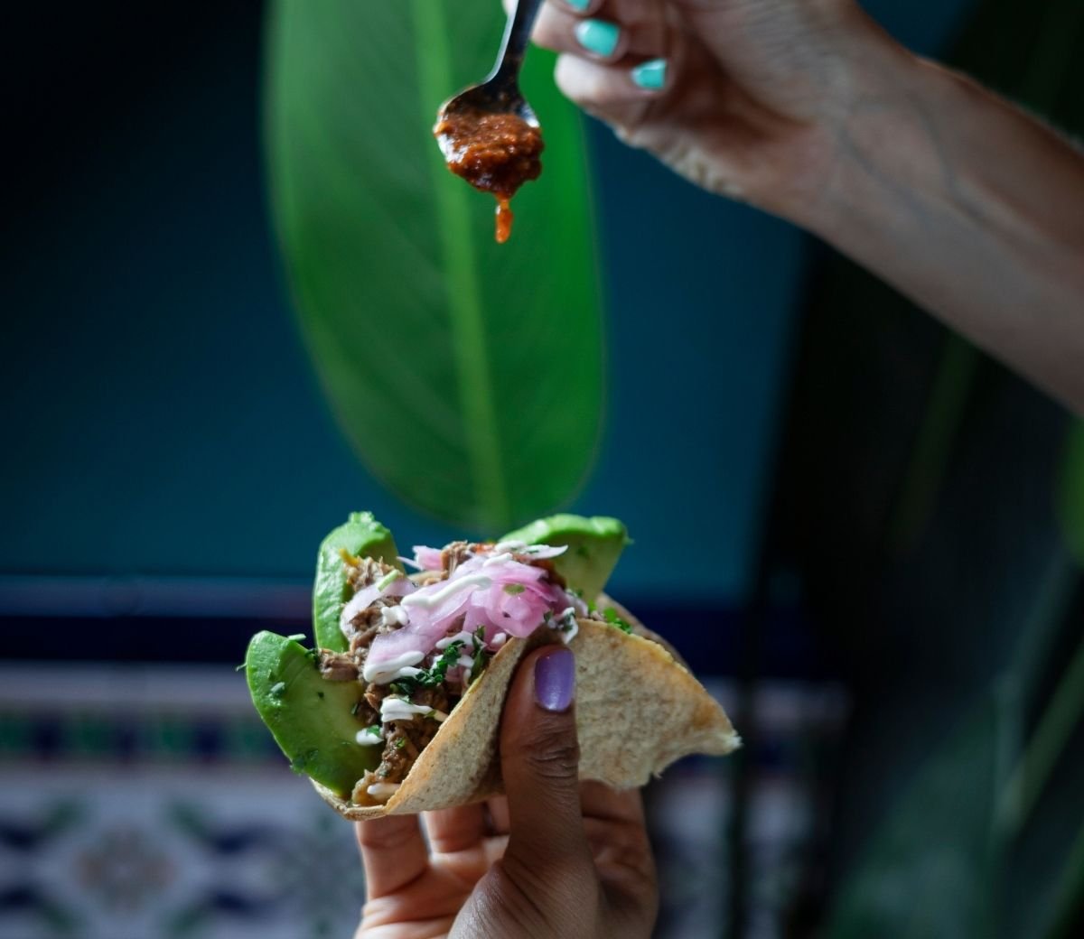 Hand holding a taco topped with guacamole and pickled red onion at Six Seis