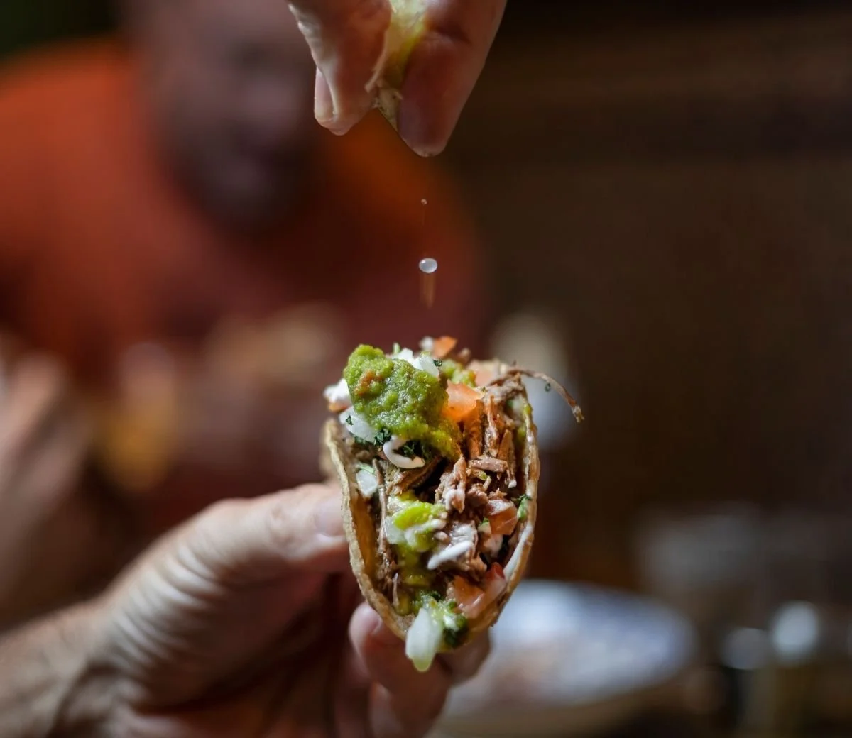 Hand holding a filled taco as lime juice is squeezed over it at Six Seis