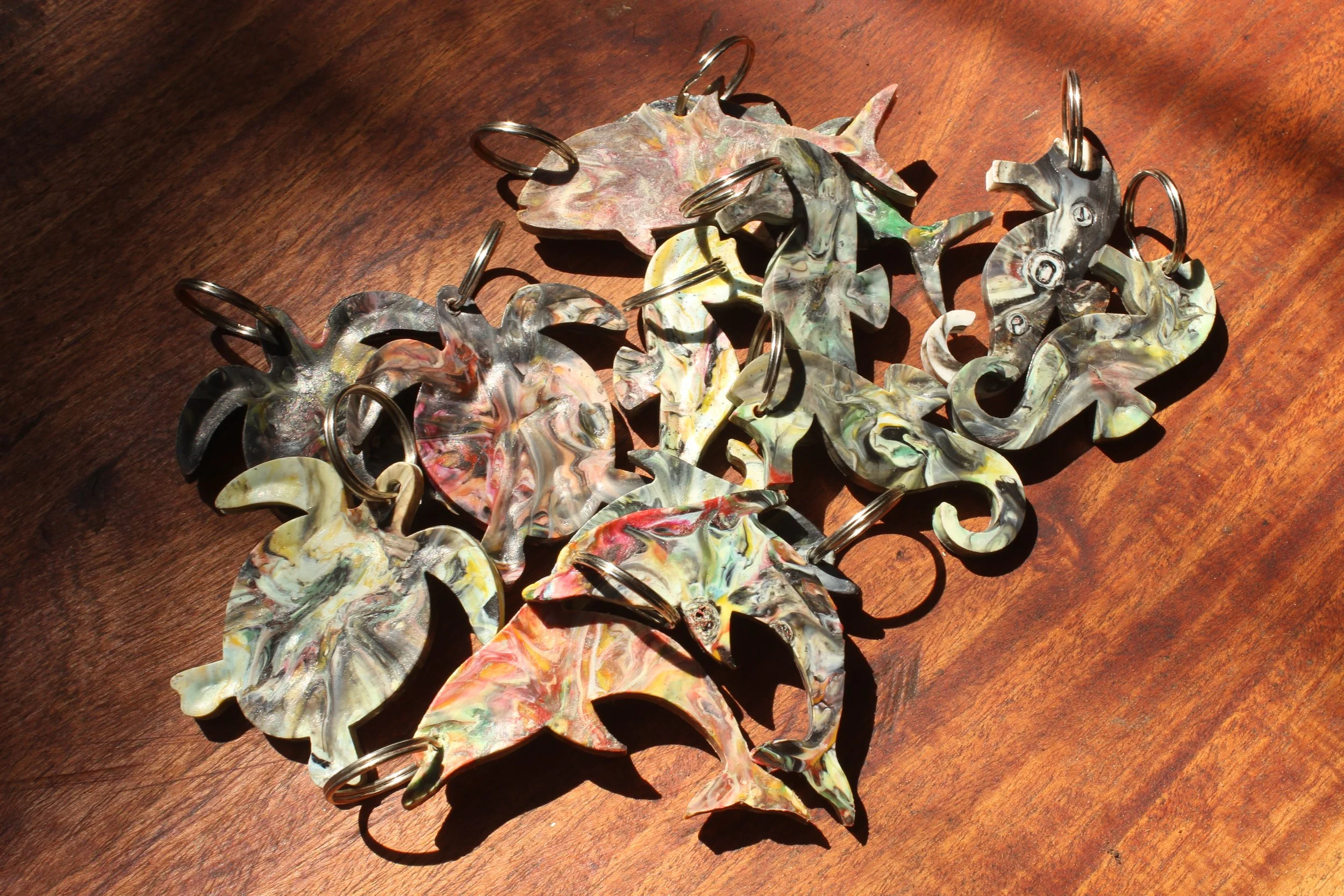 A collection of colorful, marbled, leaf-shaped earrings with silver hooks, scattered on a wooden surface in sunlight.