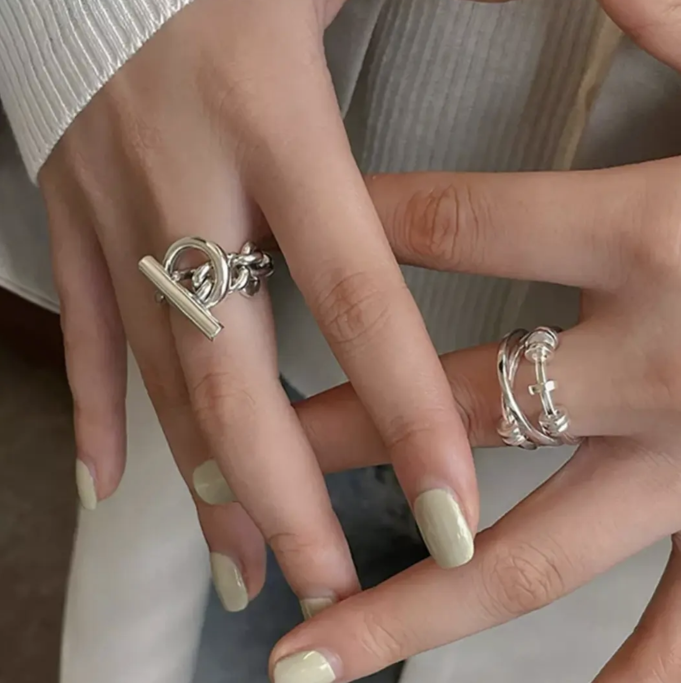 Close-up of two hands with silver rings and manicured nails, showing the rings' designs.