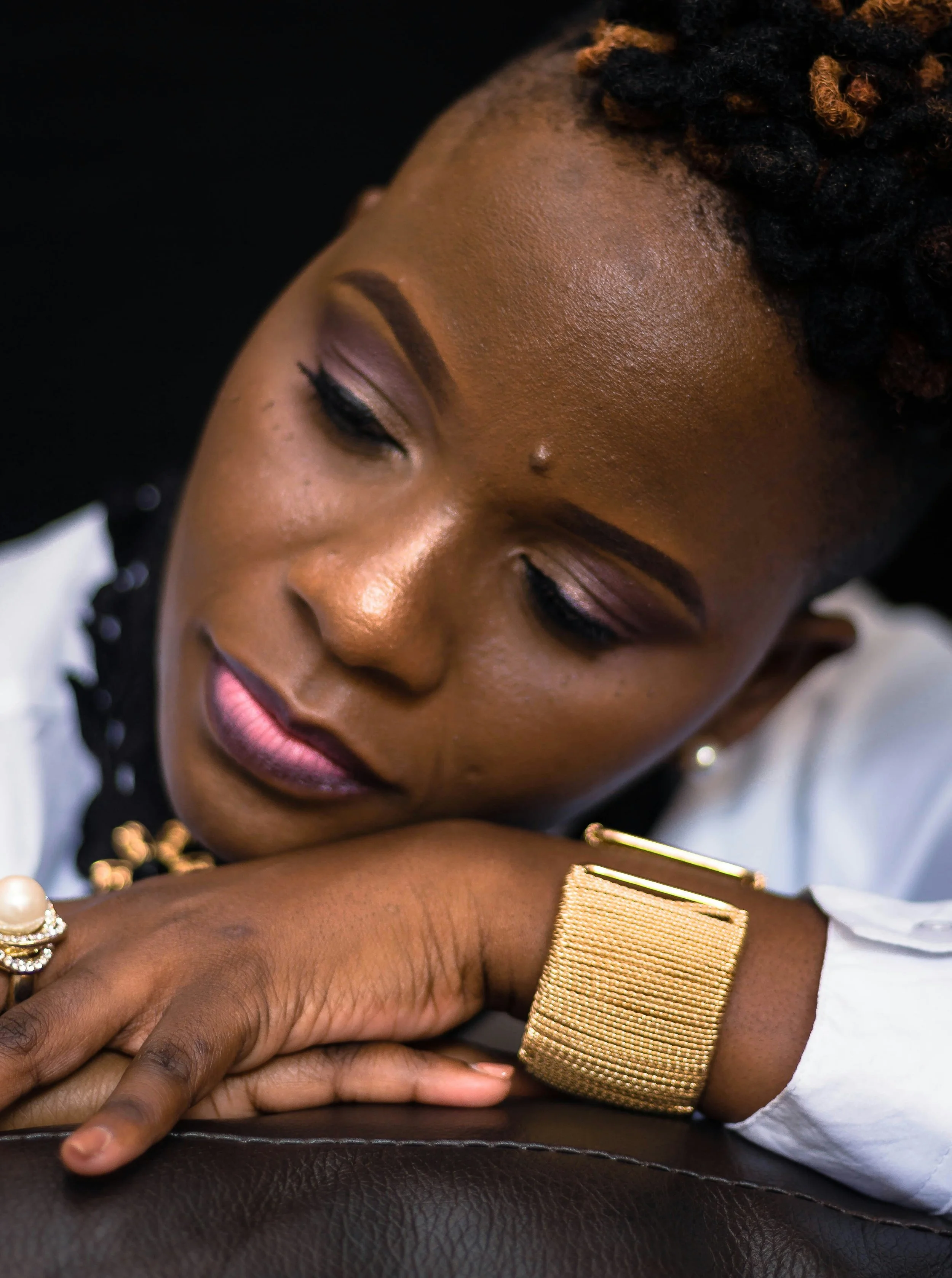 Woman resting her head on her arm, wearing a wide gold cuff bracelet and pearl ring