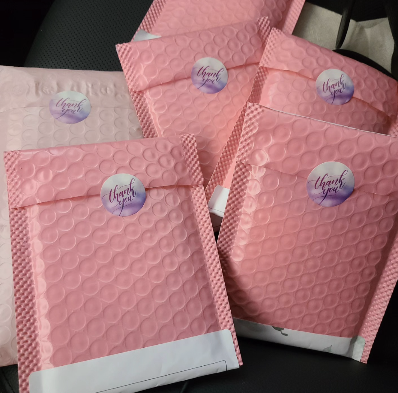Pink bubble wrap envelopes with a purple and orange 'Thank You' sticker on each, placed on a dark surface, some slightly overlapping.