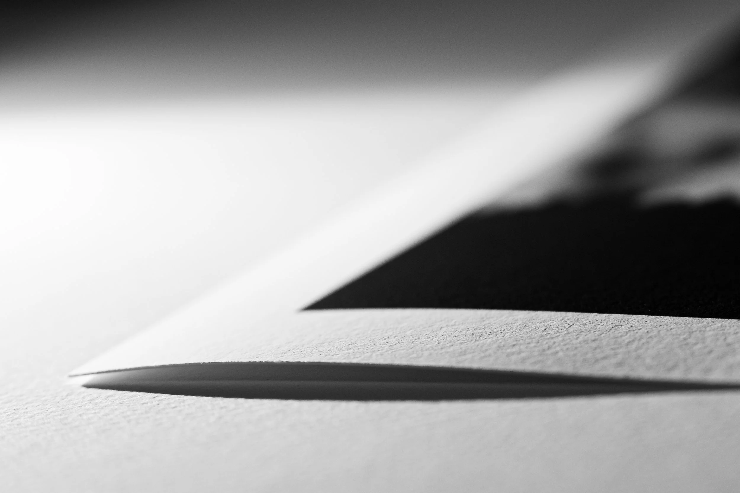 Image noire et blanc montrant une feuille de papier pliée avec son ombre sur une surface plane.