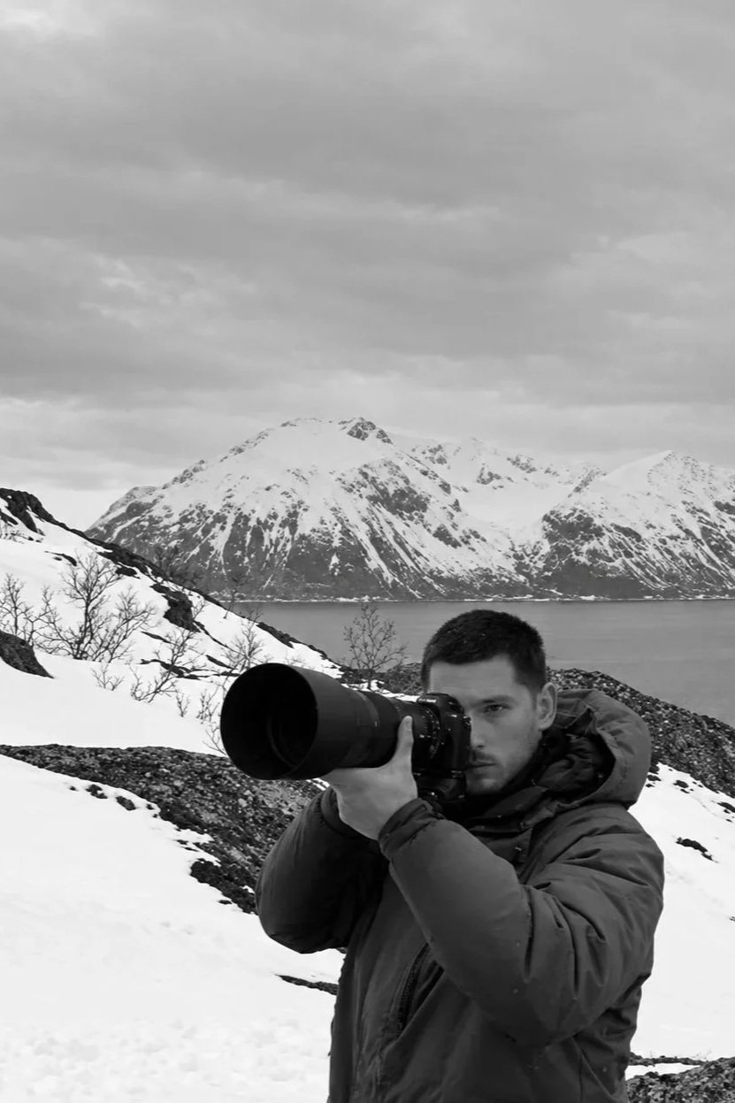 Un homme tenant un appareil photo avec un paysage montagneux enneigé en arrière-plan.