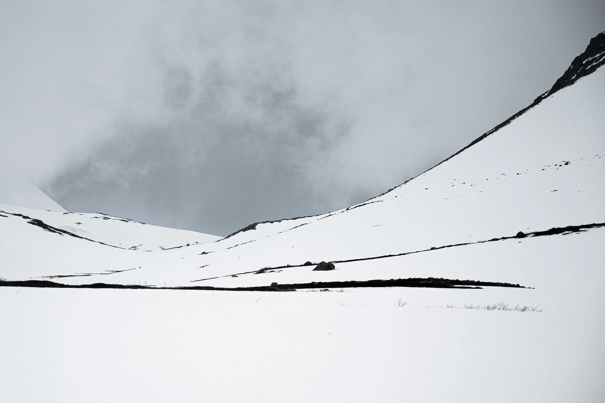 Montagne enneigée sous un ciel nuageux avec quelques rochers visibles sur la neige.