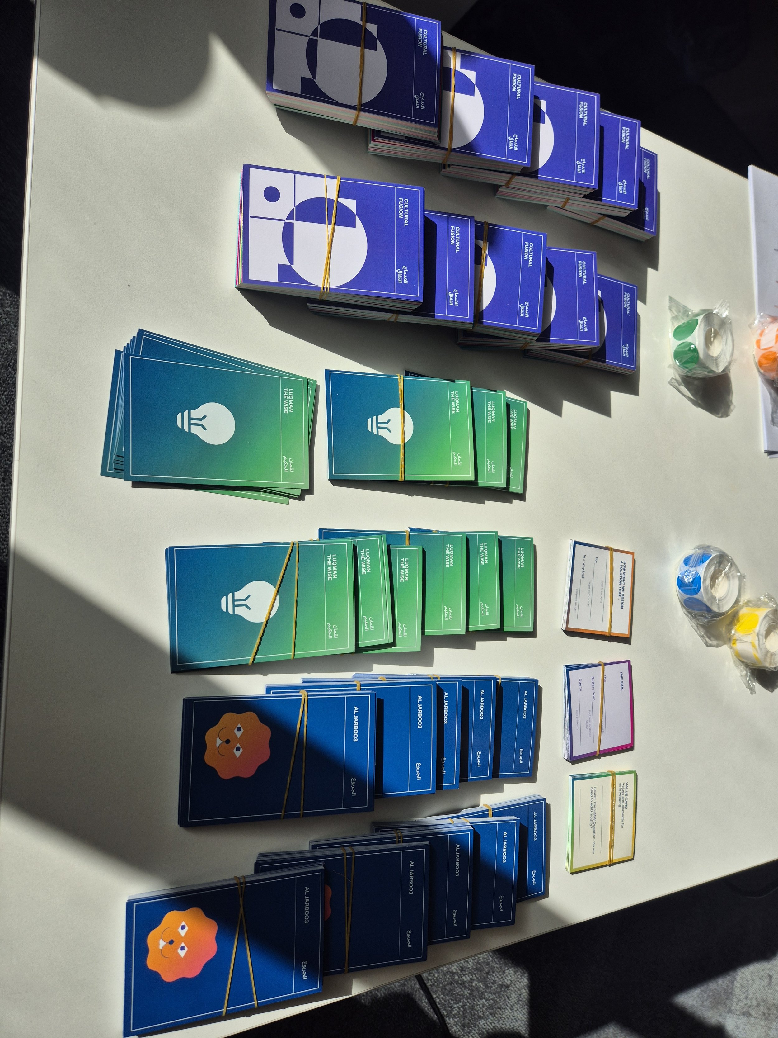 Stacks of creative ideation prompt cards in various colors (blue, green, orange, and purple) arranged on a table for an innovation workshop.