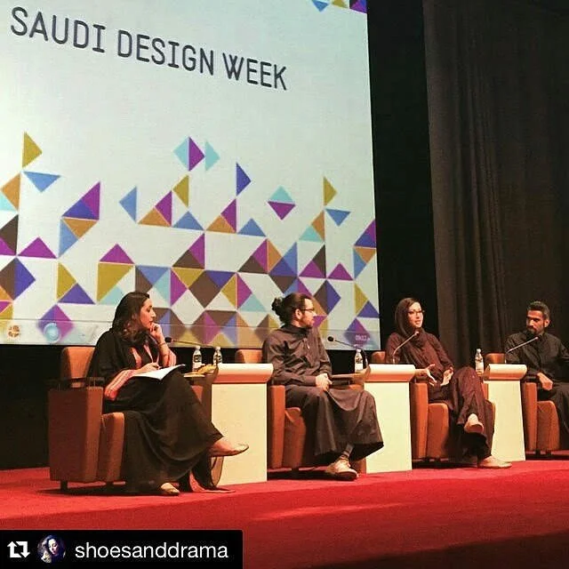 A panel discussion at Saudi Design Week with four people sitting on stage in armchairs, with a large screen behind them displaying the event name and colorful geometric patterns.