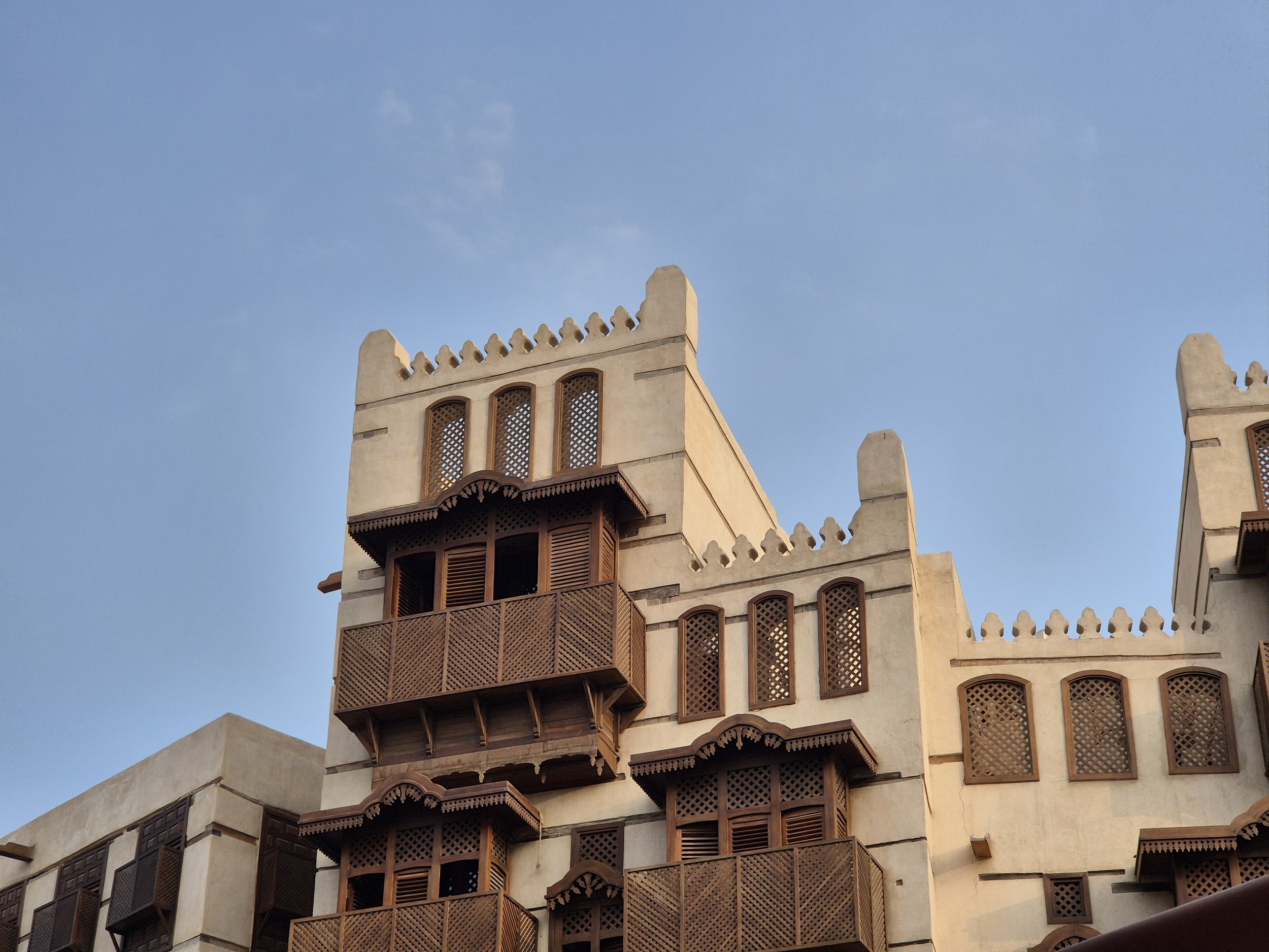 A multi-story building with traditional Middle Eastern architecture, featuring wooden lattice windows and balconies, set against a clear blue sky.