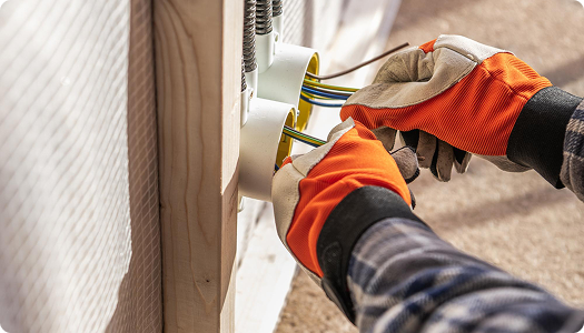 A person wearing orange gloves working on electrical wiring inside an outdoor electrical box.