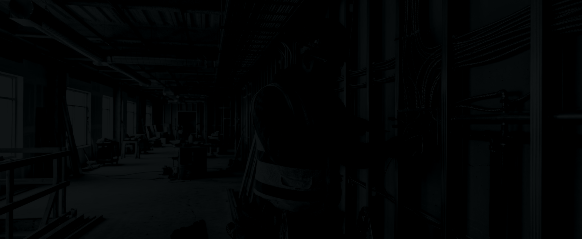 Silhouette of a worker in a construction or industrial setting, working on electrical wiring inside a building under construction.