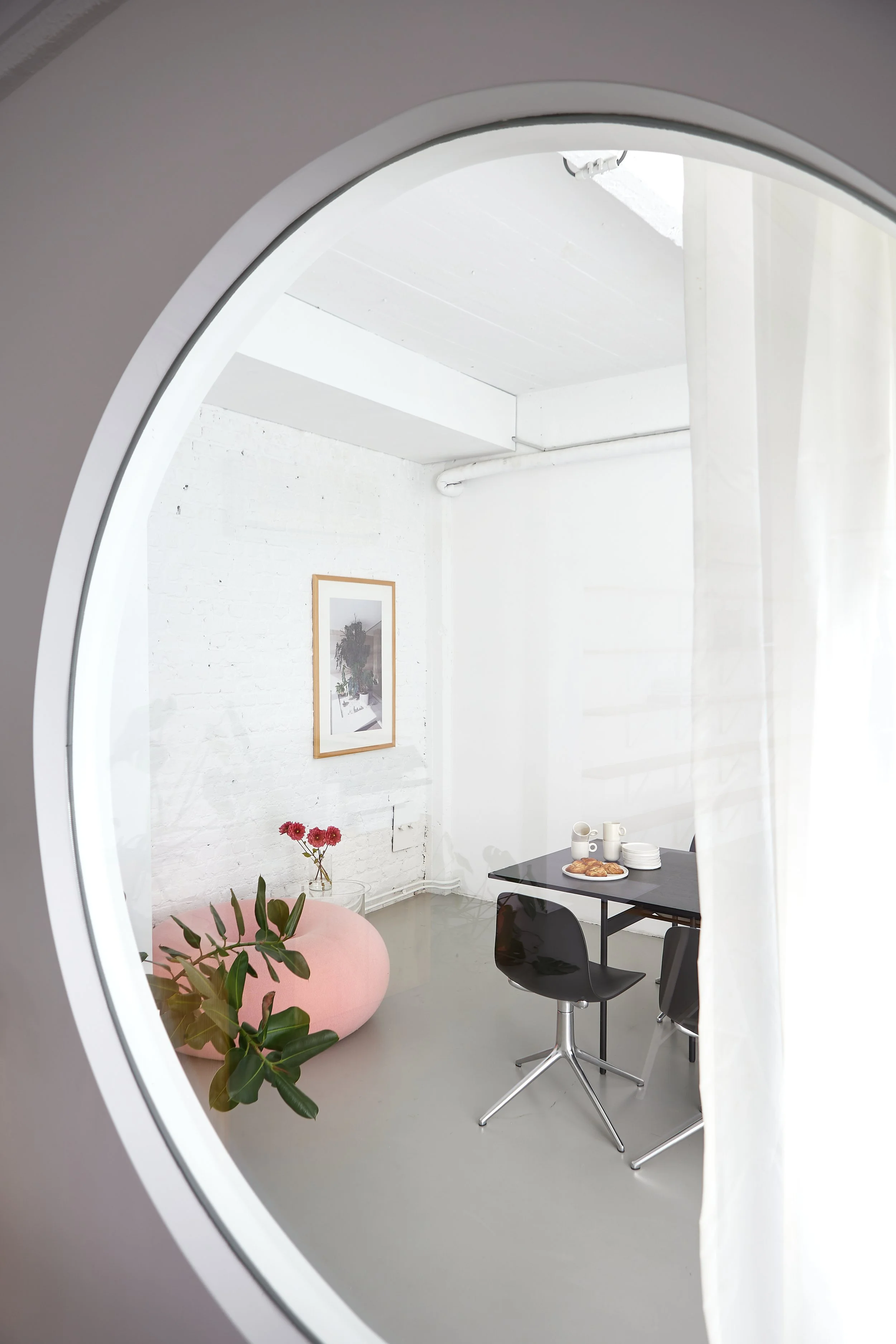 Interieur van een minimalistisch, modern eet- of vergaderruimte met witgekaleerde muren, een zwart tafel met stoelen, en een antwoord op de muur. Er staat een vaas met bloemen en een dienblad met ontbijt of snacks op de tafel.