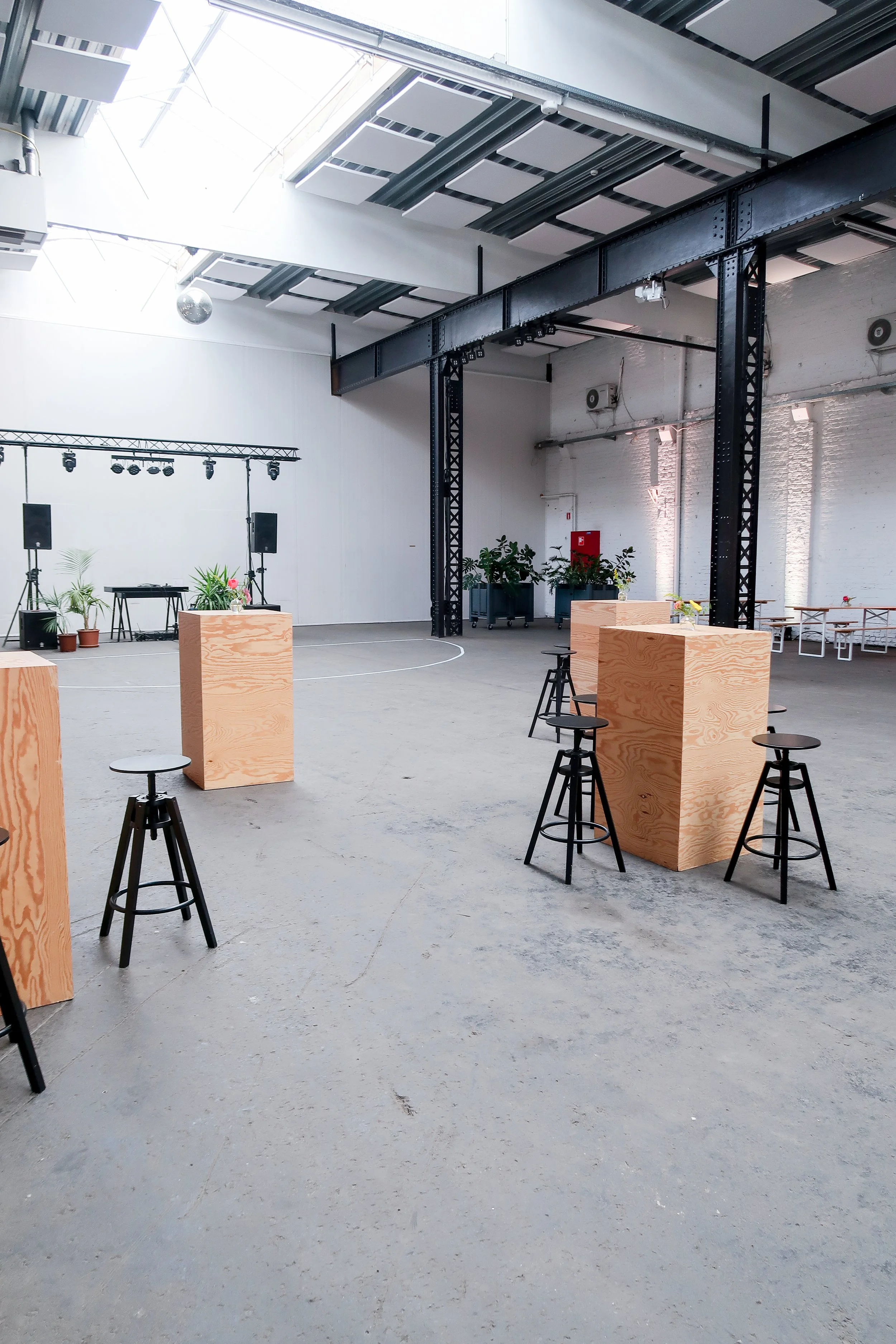 Een lege industriele ruimte die is ingericht voor een evenement of feest, met houten objecten, planten, geluidssystemen en een lichtinstallatie.
