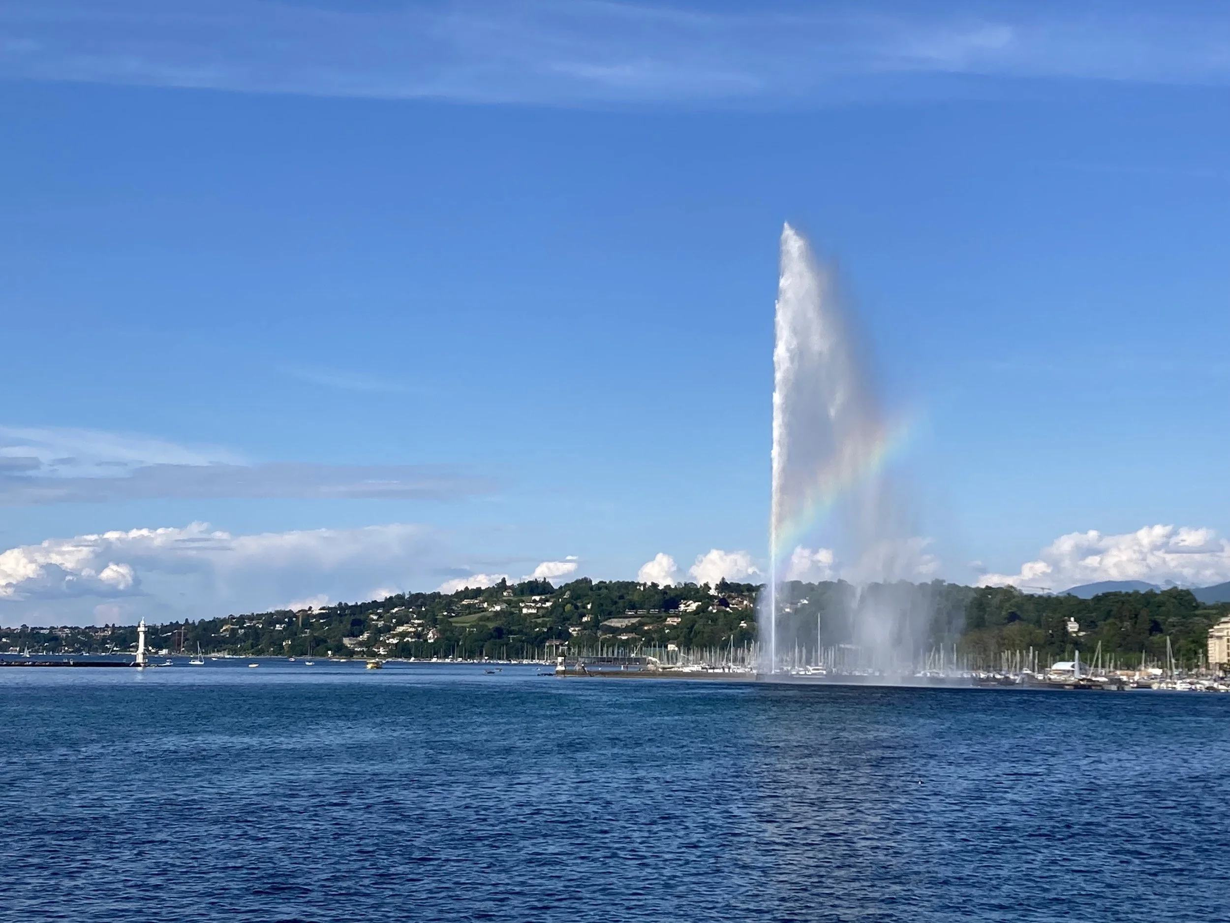 A Jet d’Eau fountain in Geneva with a rainbow in the spray and Lake Geneva in the foreground.