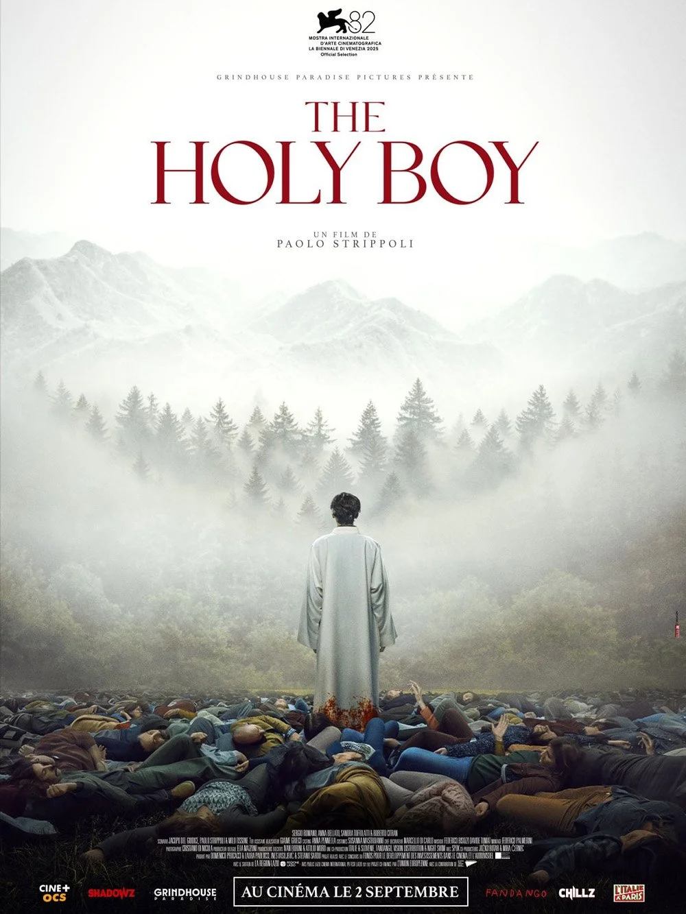 Affiche du film 'The Holy Boy' montrant un paysage montagneux en arrière-plan, un homme en robe blanche au centre, entouré de nombreux corps au sol, avec le titre du film en haut.