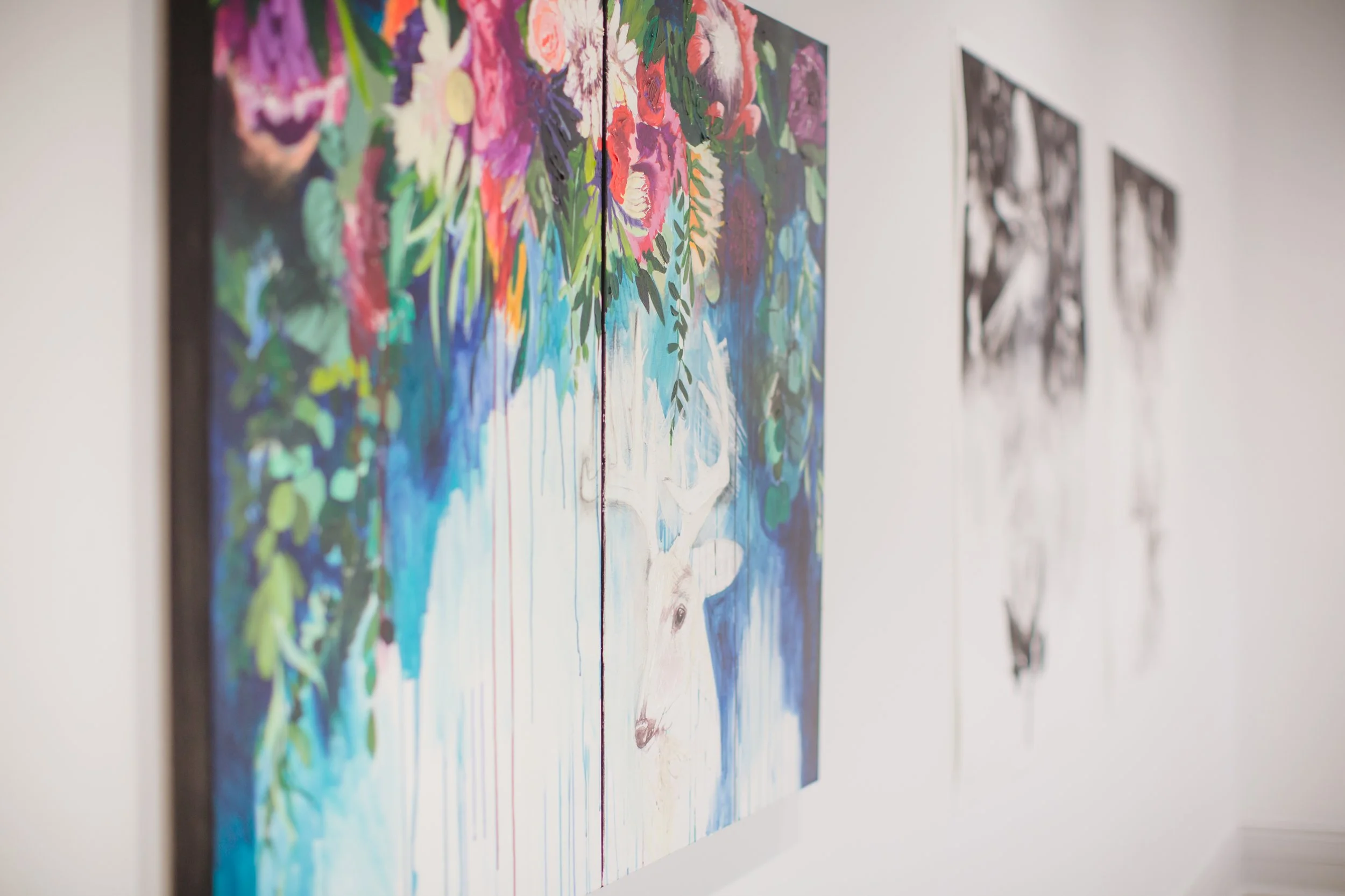 Close-up of colorful abstract floral paintings hanging on a white gallery wall.