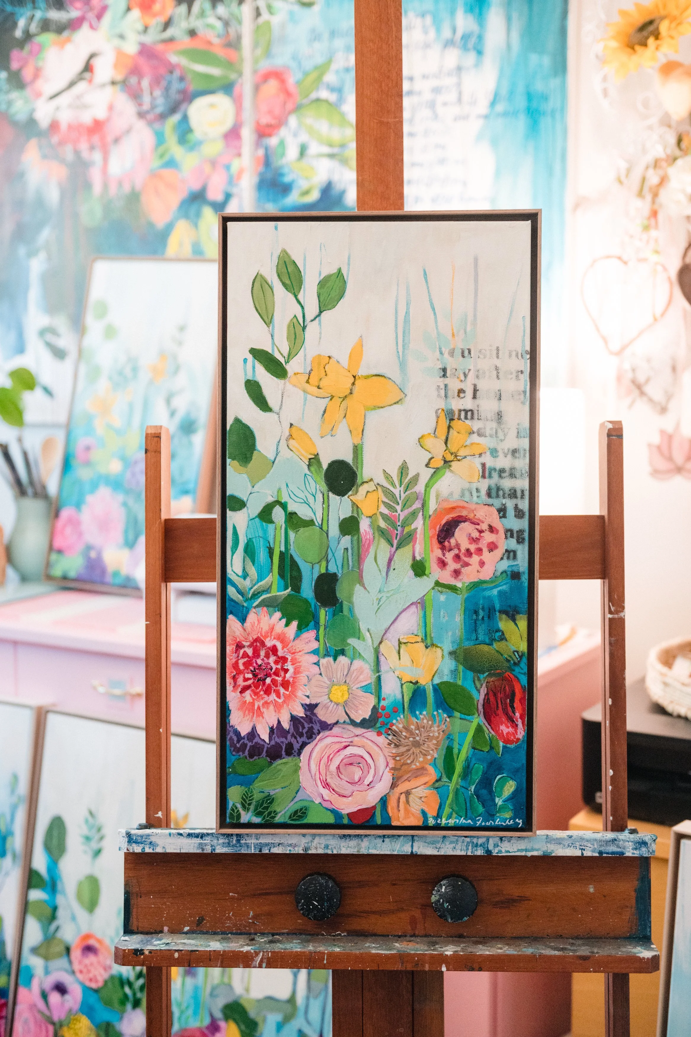 A colorful painting of various flowers and leaves in a vibrant, abstract style, displayed on an easel in an art gallery.