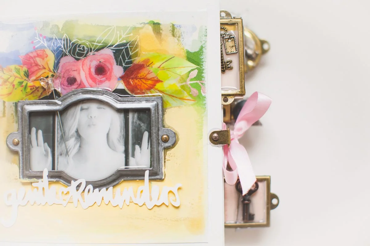 A scrapbook page with a black-and-white photo of a woman making a peace sign, surrounded by colorful floral decorations, with the partially visible words 'gentle Reminders,' and buttons and a pink ribbon tied in a bow on the side.