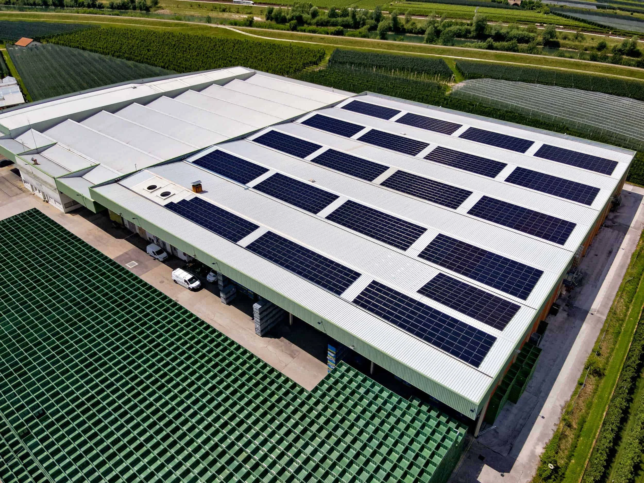 Luftaufnahme eines Gebäudes mit Solarpaneelen auf dem Dach, umgeben von landwirtschaftlichen Flächen und Gärten.