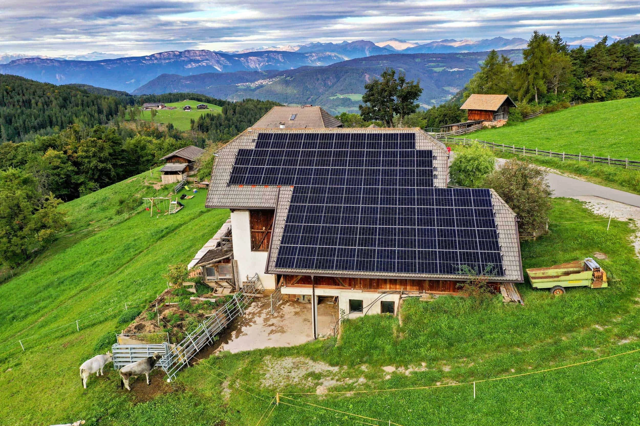 Haus mit Solardach in einer grünen bergigen Landschaft mit kuielnden Bergen im Hintergrund.