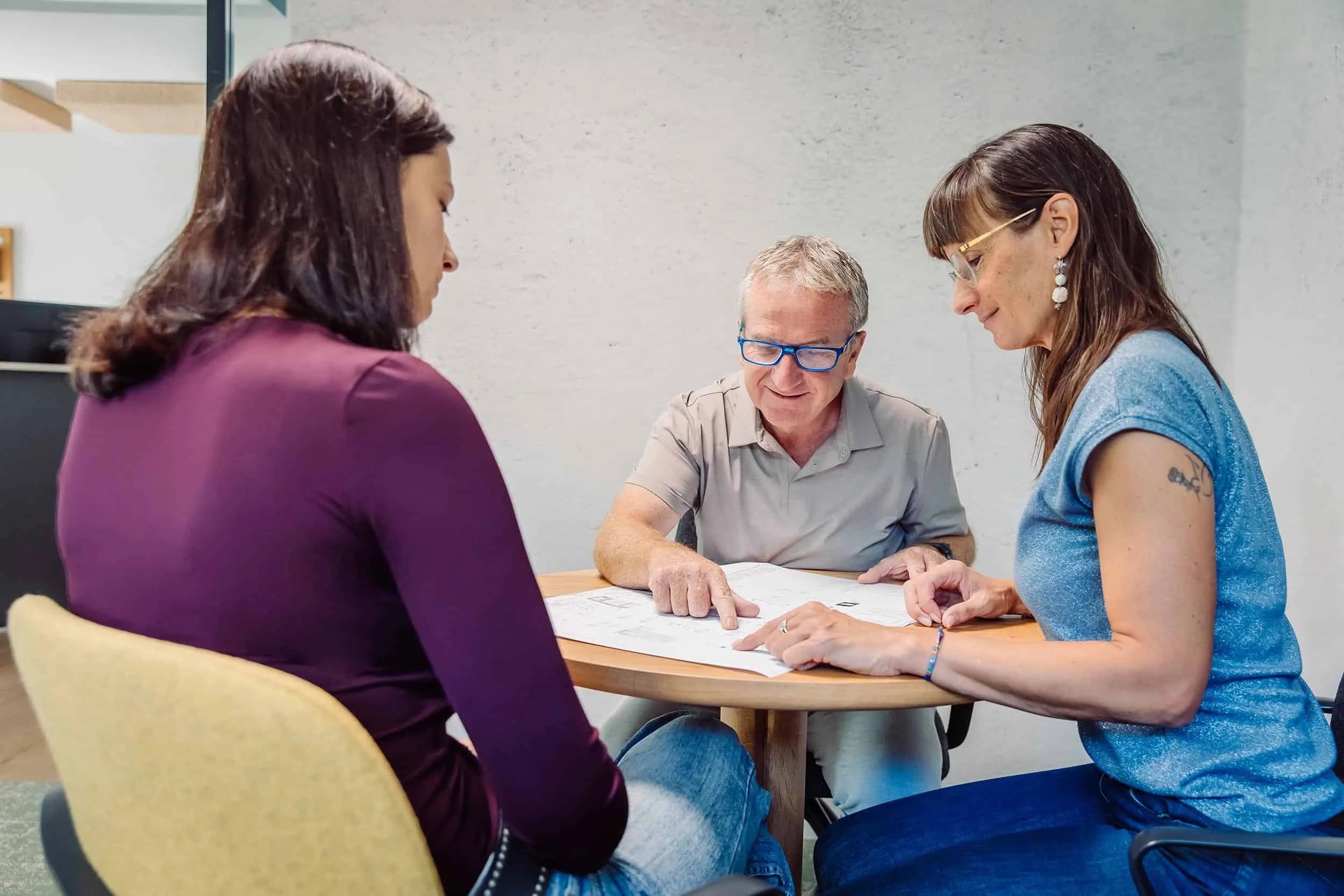 Drei Frauen und ein Mann sitzen an einem Tisch und lesen gemeinsam Dokumente in einem Büro.