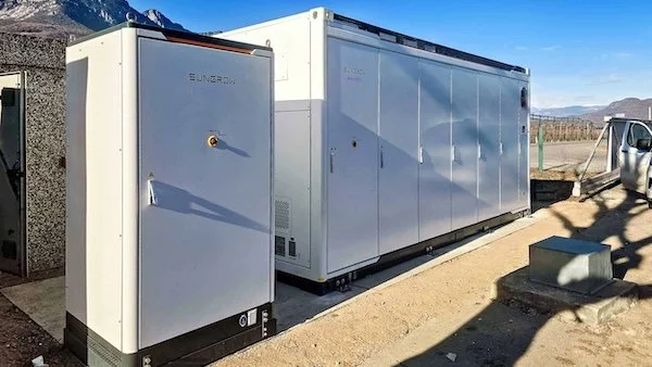 Großes industrielles Elektronikgerät im Freien, vermutlich ein Kältesystem oder eine Klimaanlage, auf einer Betonbasis mit umliegender Landschaft und Fahrzeug im Hintergrund.