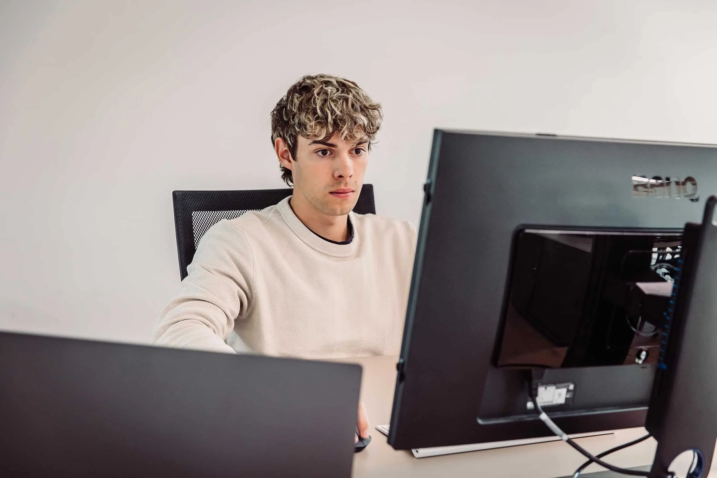 Ein junger Mann arbeitet an einem Computer in einem Büro, umgeben von mehreren Monitoren.