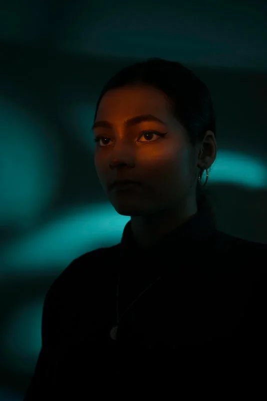 A dark portrait of a a young woman against a mysteriously lit greenish backdrop.