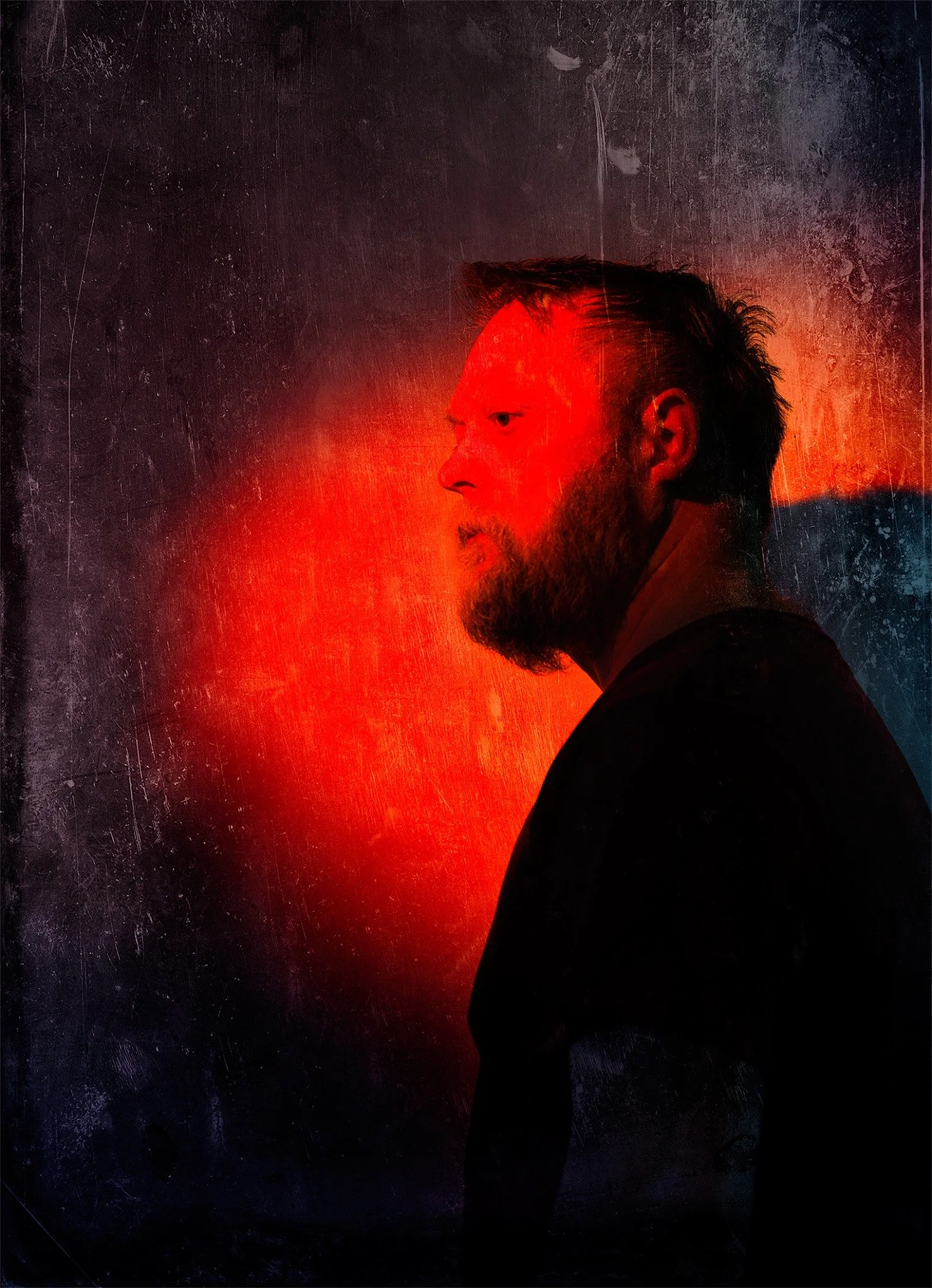 Profile photo of a bearded man in red light.