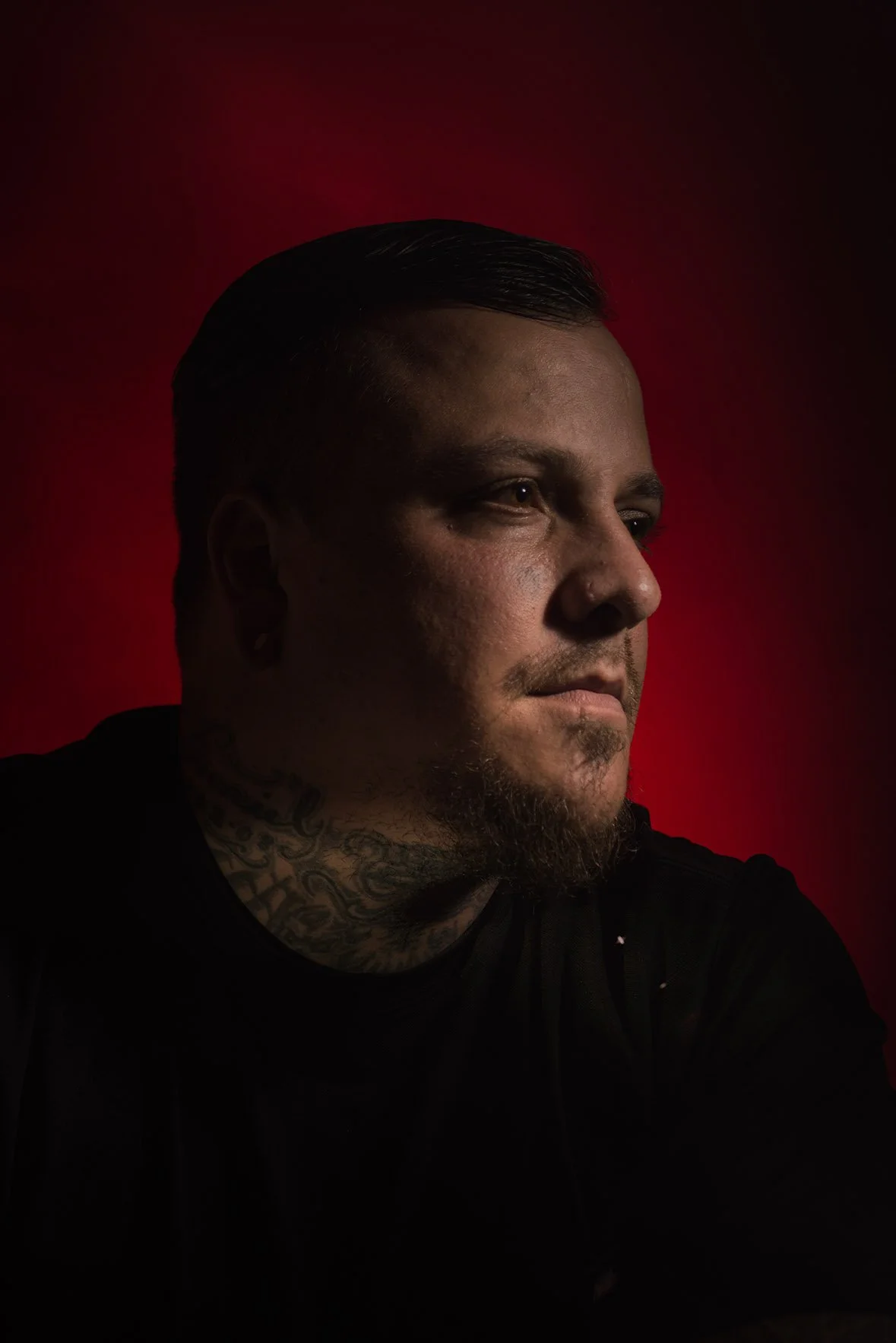 A profile portrait of a man with a tattoo on his neck.