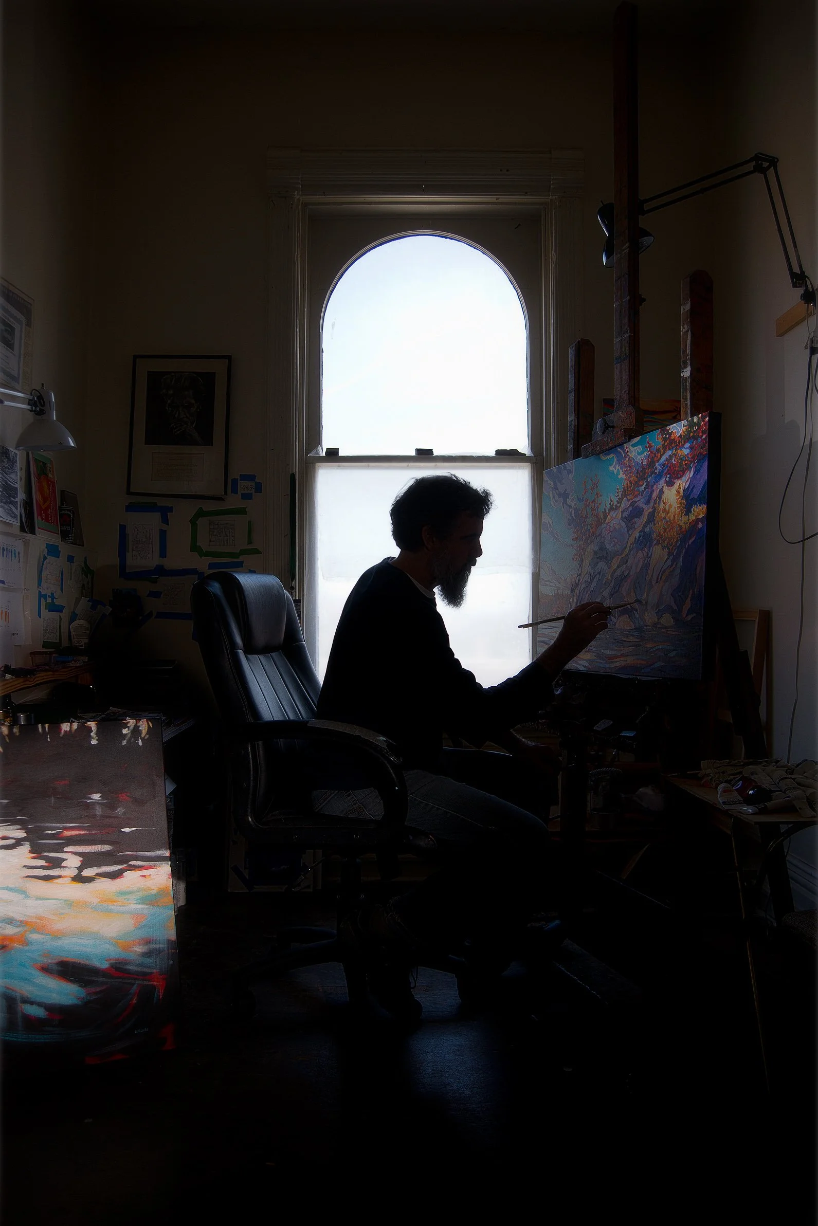 A backlit portrait of a man painting a picture.