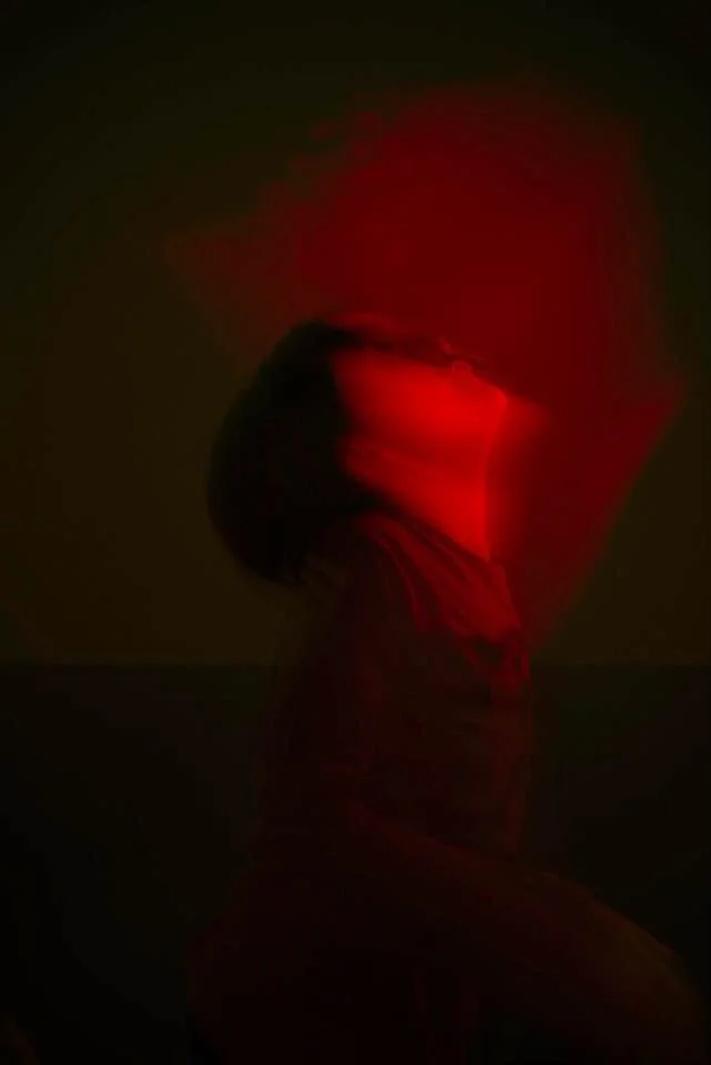 A dark portrait of a young person in red light.