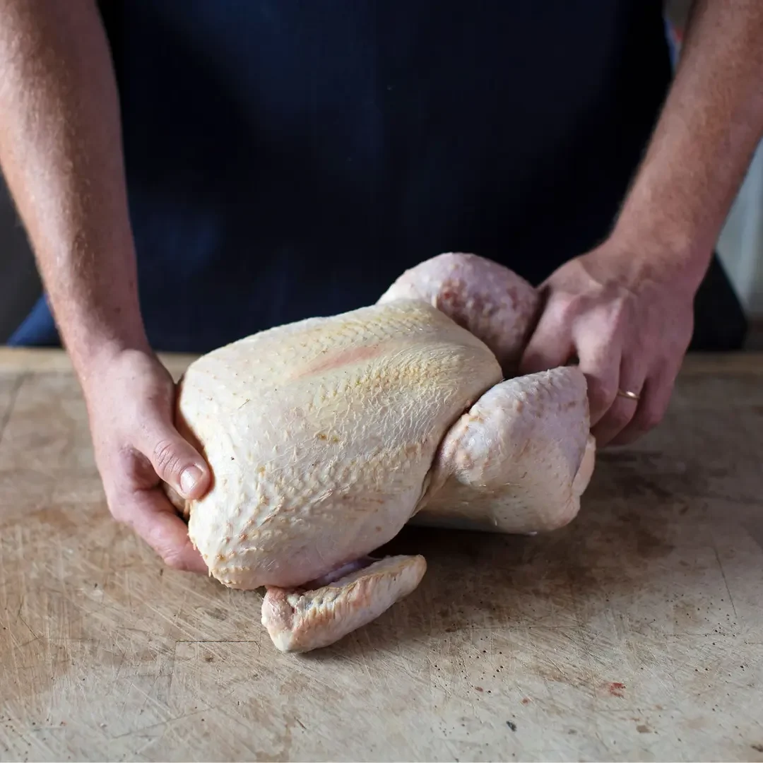 hands holding a raw chicken on a wooden board