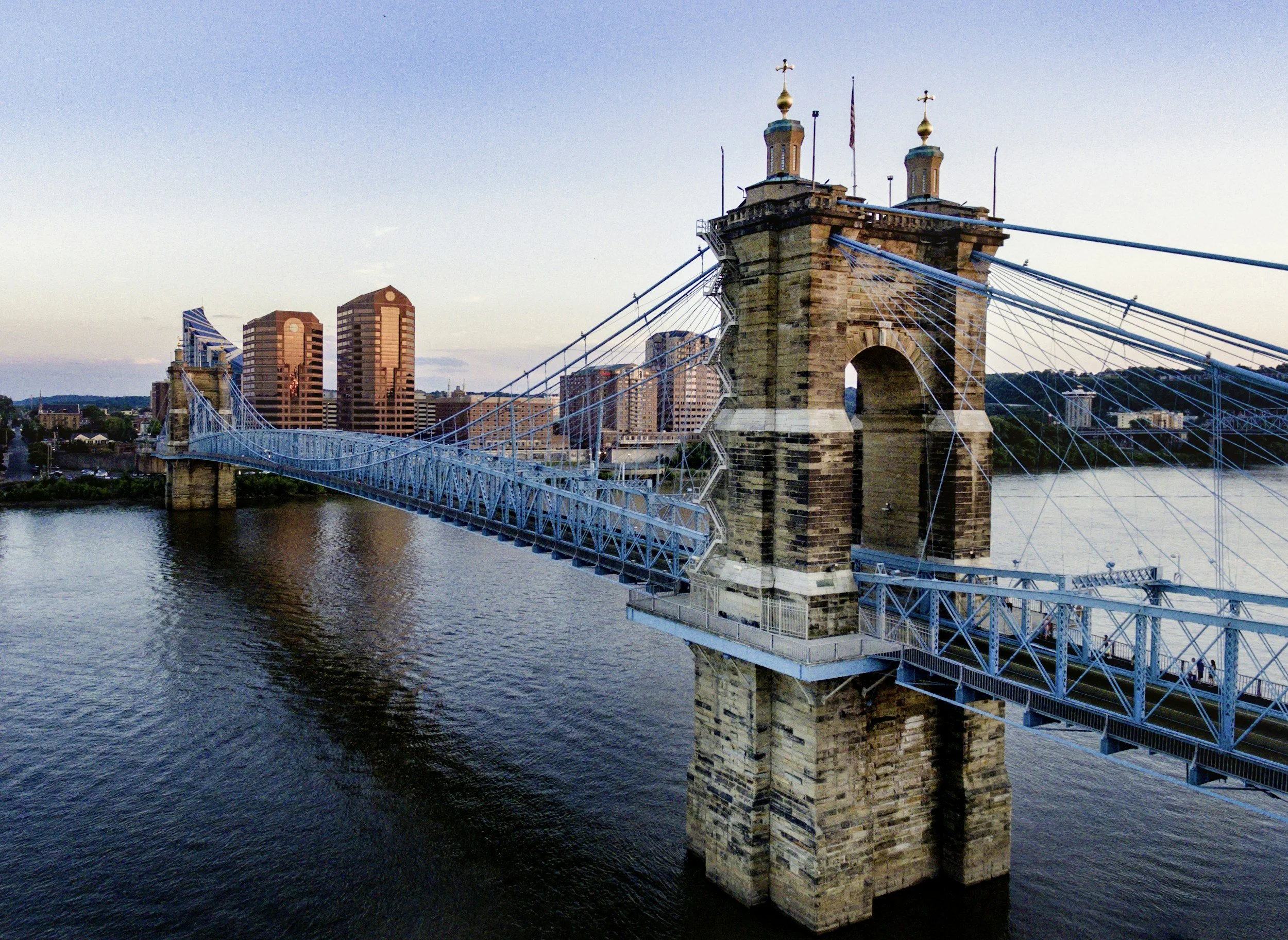 A bridge over a river with a city skyline in the background, featuring tall buildings and a clear sky.