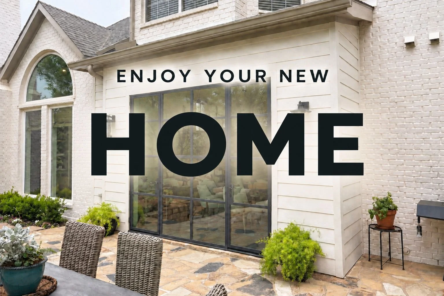 A backyard patio with a white brick house, outdoor table and chairs, potted plants, and large windows. Overlaid text says, 'Enjoy your new home.'
