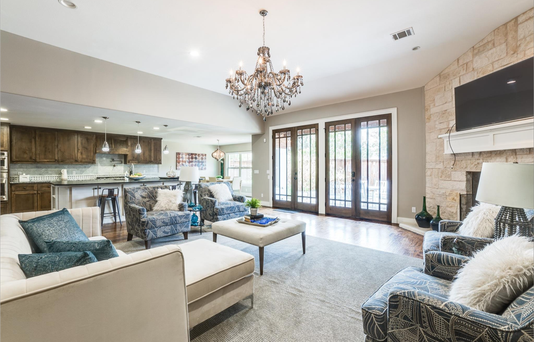 Open-concept living room and kitchen with neutral tones, a chandelier, and French doors leading outside.