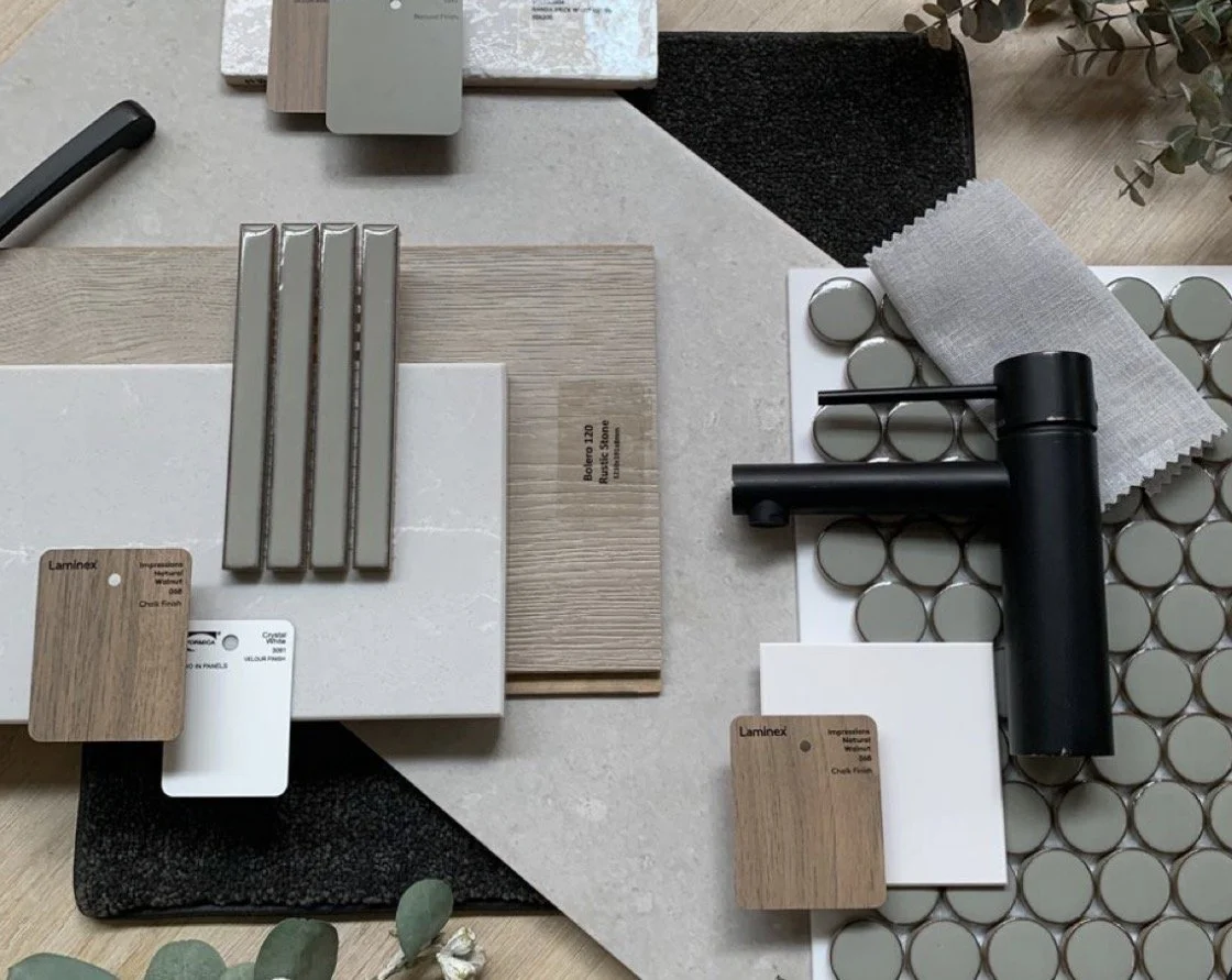 A table displays various tiles, samples, and tools for a tiling or flooring project, including small round tiles, large tiles, color and texture samples, and a black hand-held grout or sealant applicator.