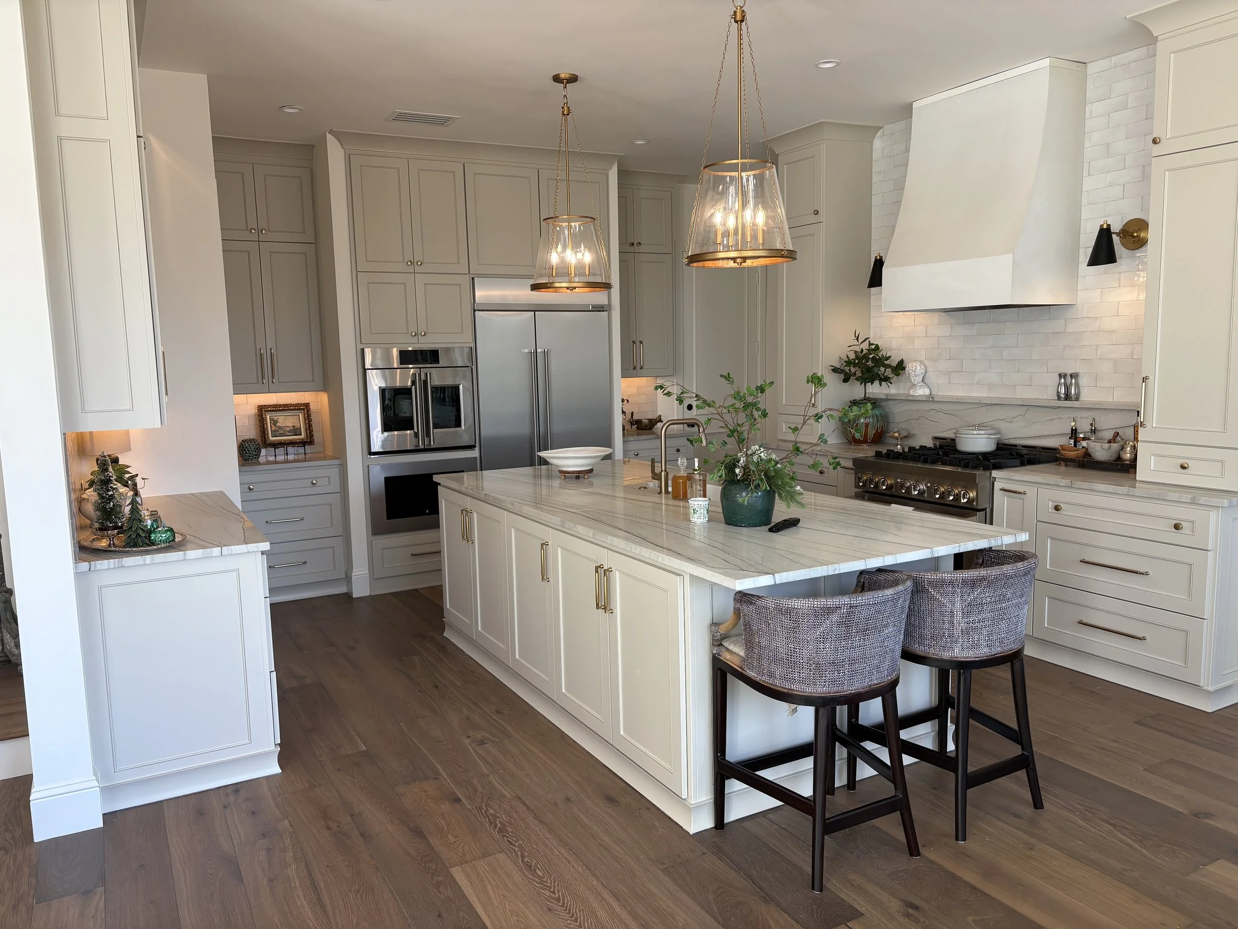 A modern kitchen with white cabinetry, stainless steel appliances, a marble island, and warm lighting fixtures.