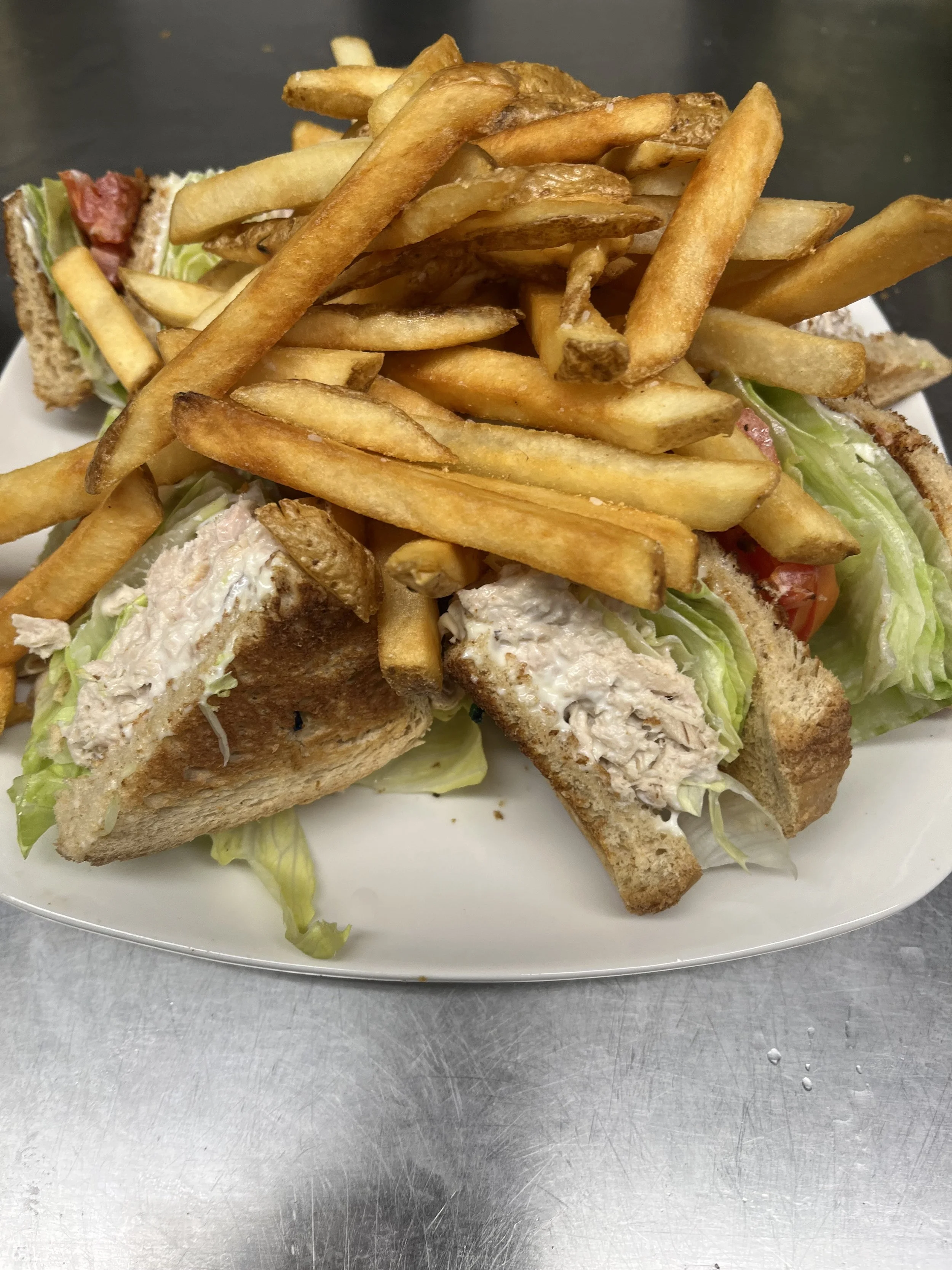 A plate with a sandwich cut in half, containing lettuce, tomato, and chicken salad, topped with French fries.