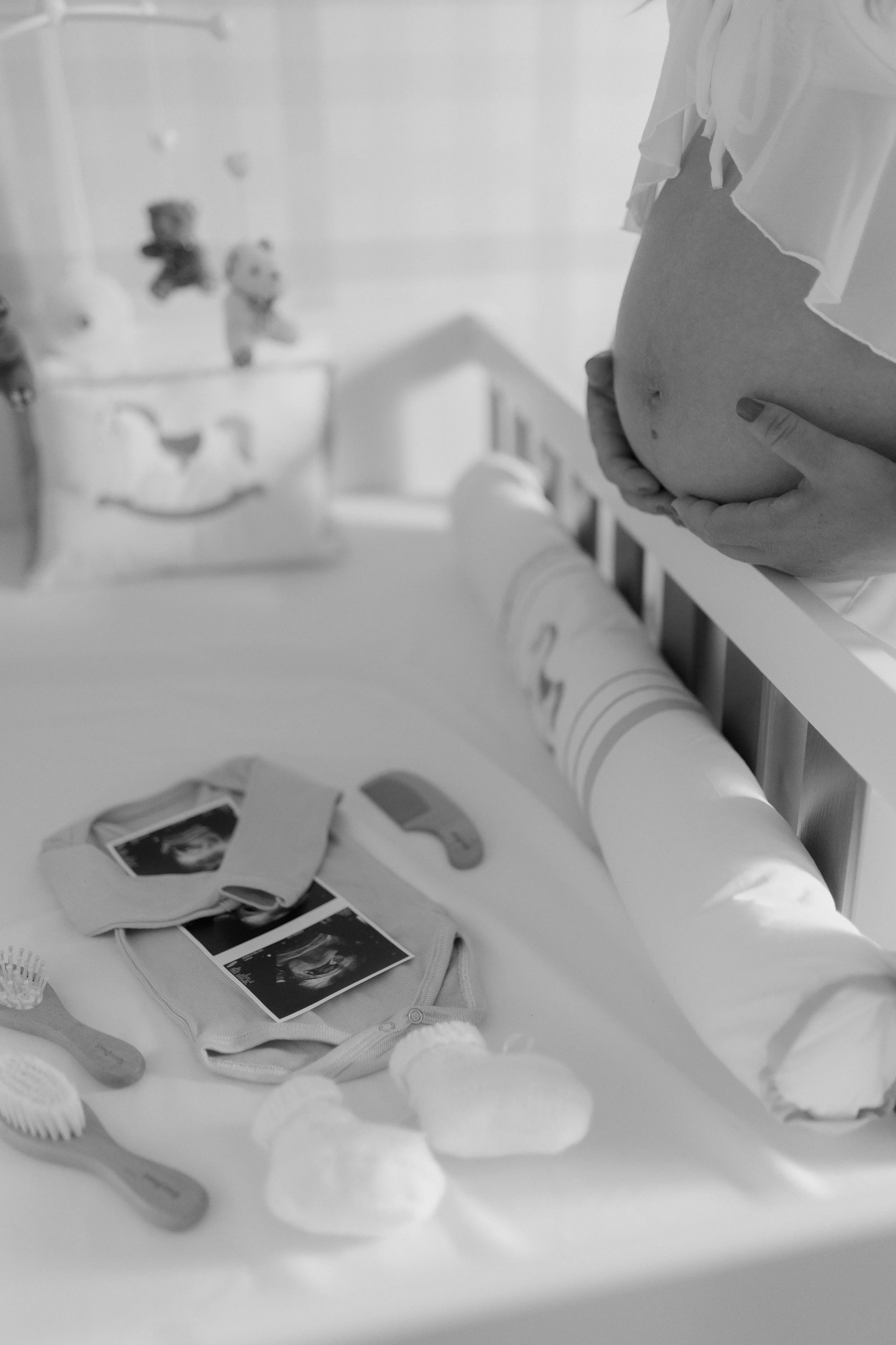 Pregnant woman holding her belly beside baby clothes, ultrasound photos, and a teddy bear