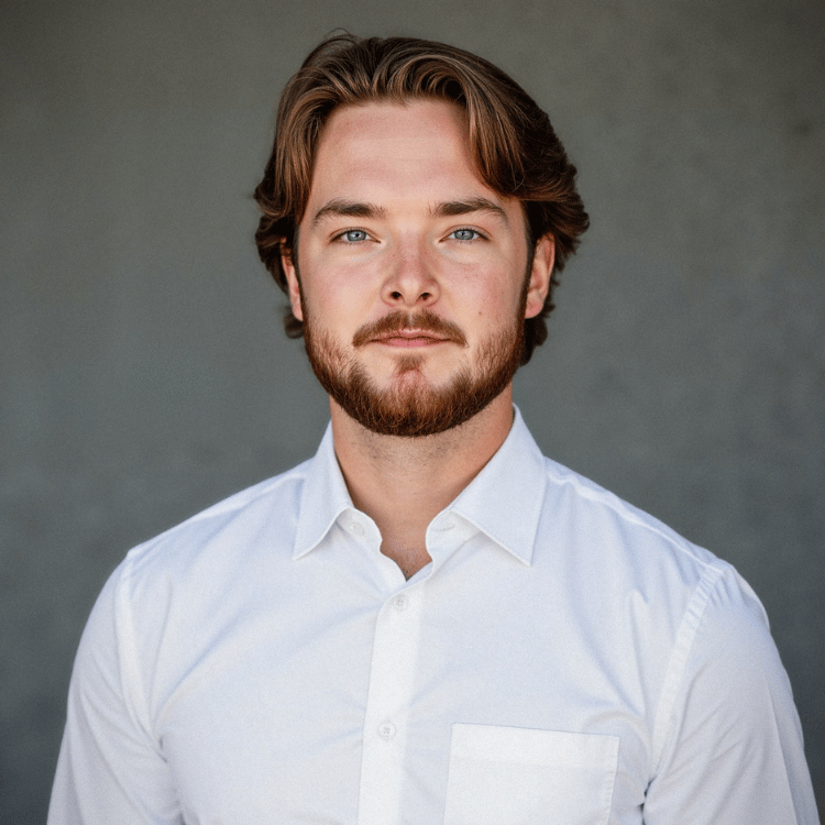 Headshot of a young man with brown hair, blue eyes, and a beard, wearing a white button-up shirt against a gray background.