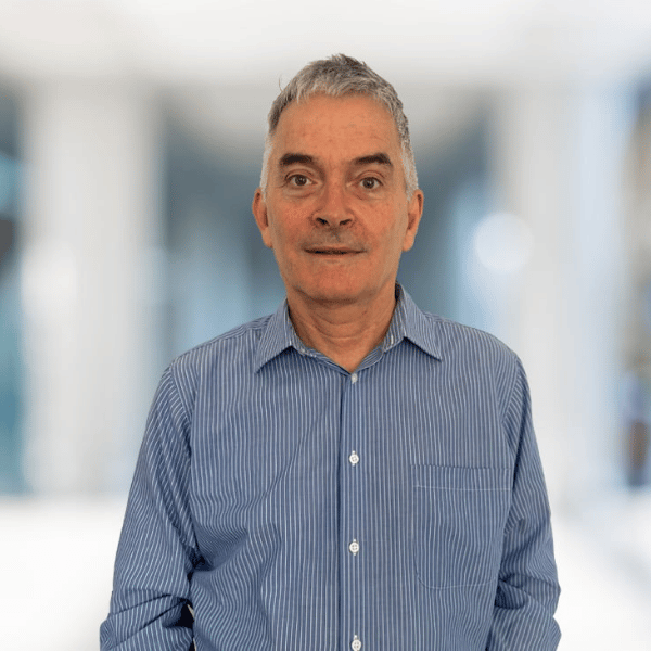A middle-aged man with short gray hair wearing a blue striped button-up shirt standing in a brightly lit indoor space with large windows.