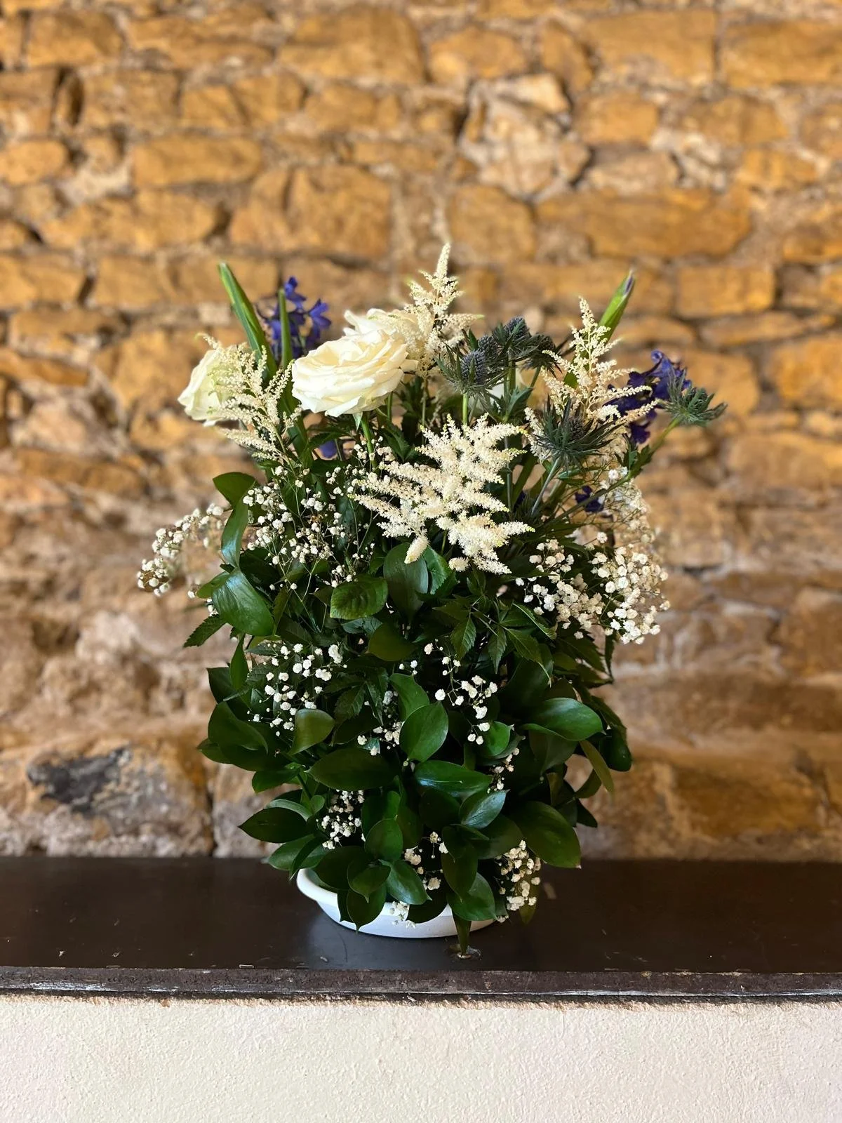 Bouquet de fleurs blanches et violettes avec un mur en pierre en arrière-plan.