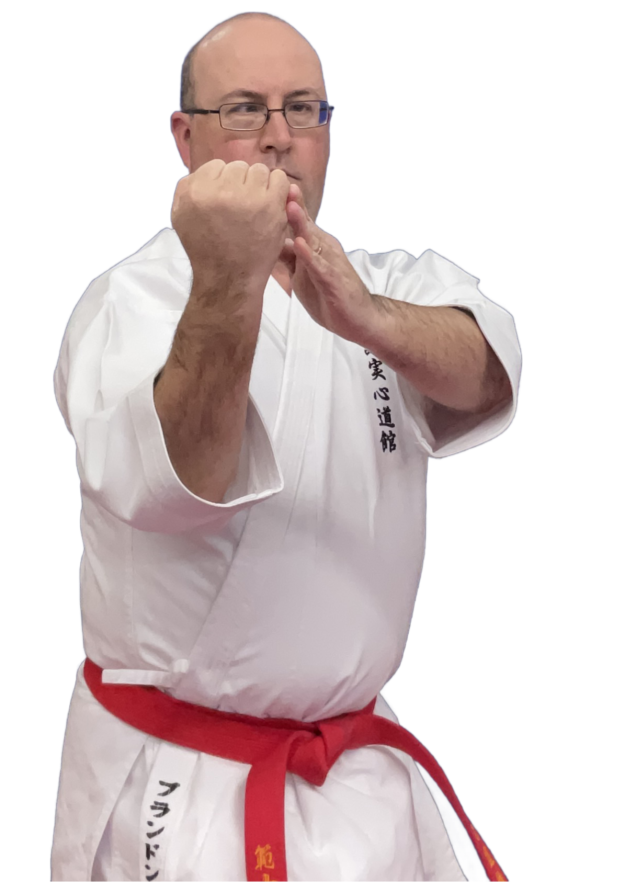 A man in a karate uniform performing a martial arts pose with his fists raised. He wears glasses and a white gi with Japanese characters and a red belt.