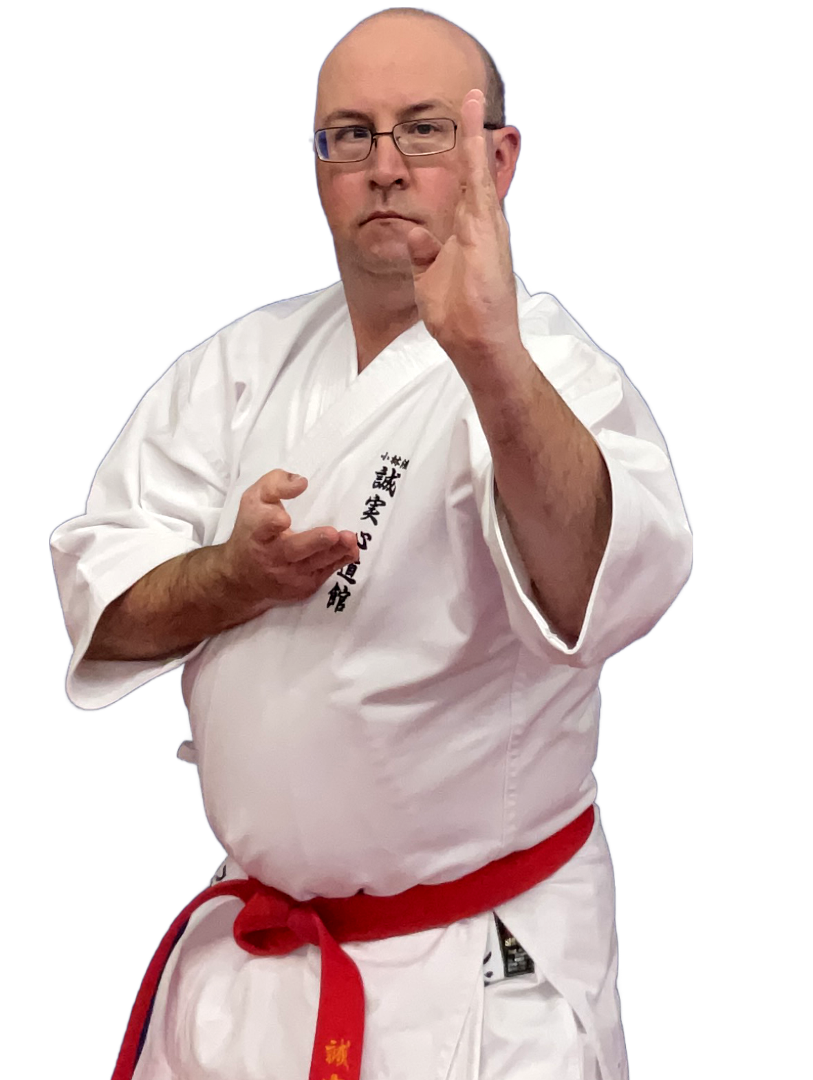 A man in a white karate gi with black Japanese characters on the left side, wearing glasses, making a martial arts stance with one hand in a fist and the other hand open, against a black background.